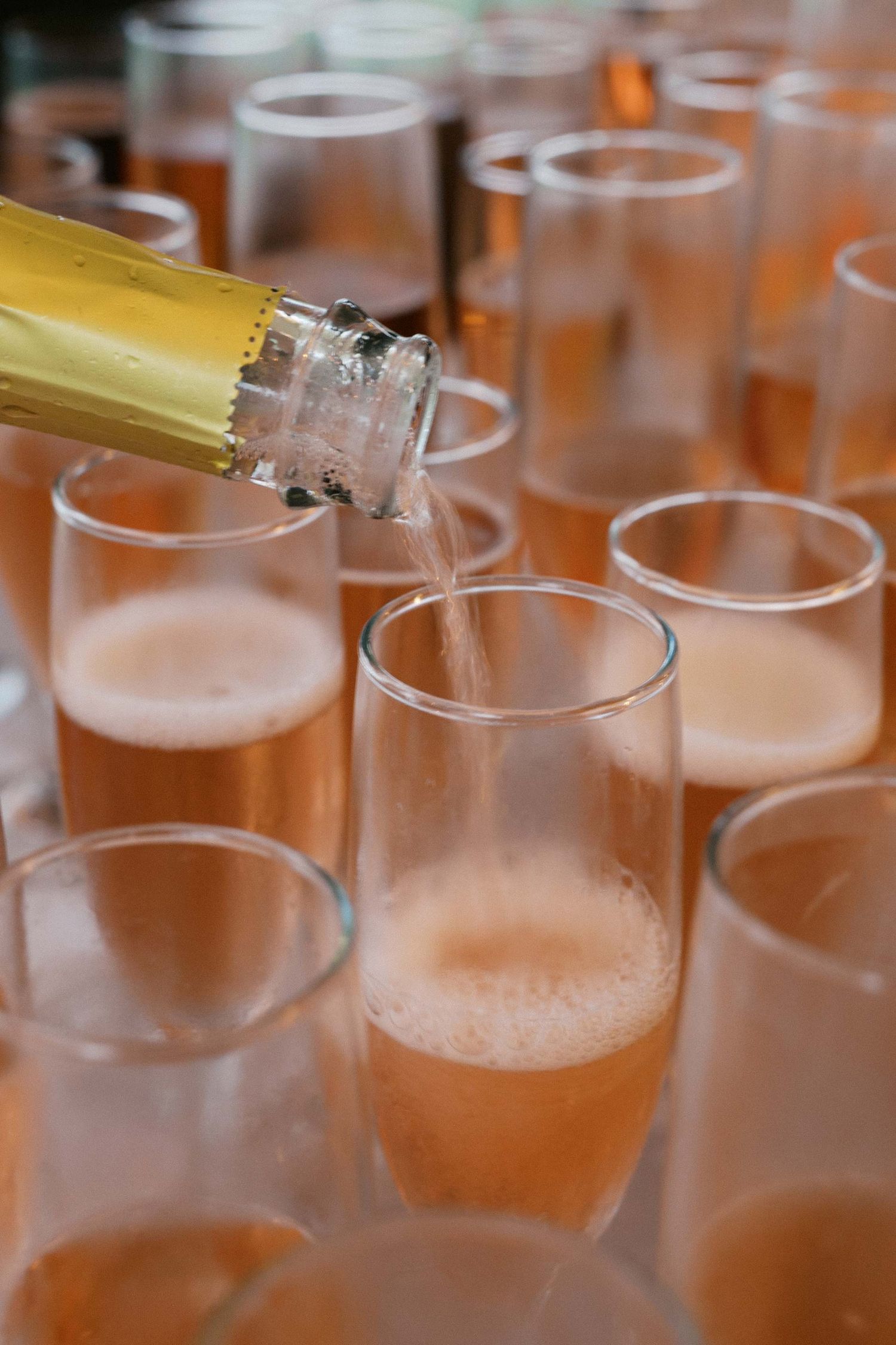Closeup view of champagne being poured into multiple glass flutes at a wedding celebration.