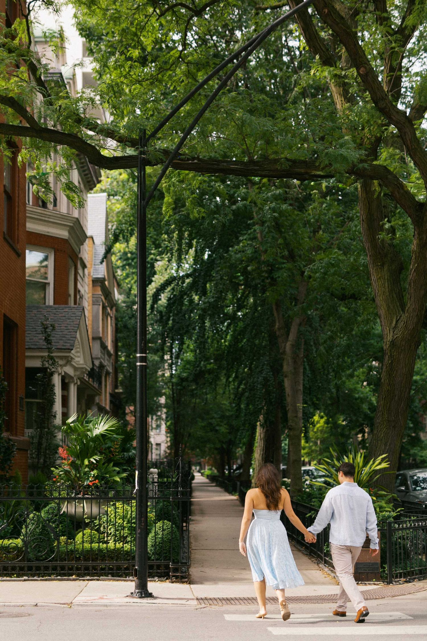 Couple walking hand in hand down a tree-lined sidewalk in a charming urban neighborhood.