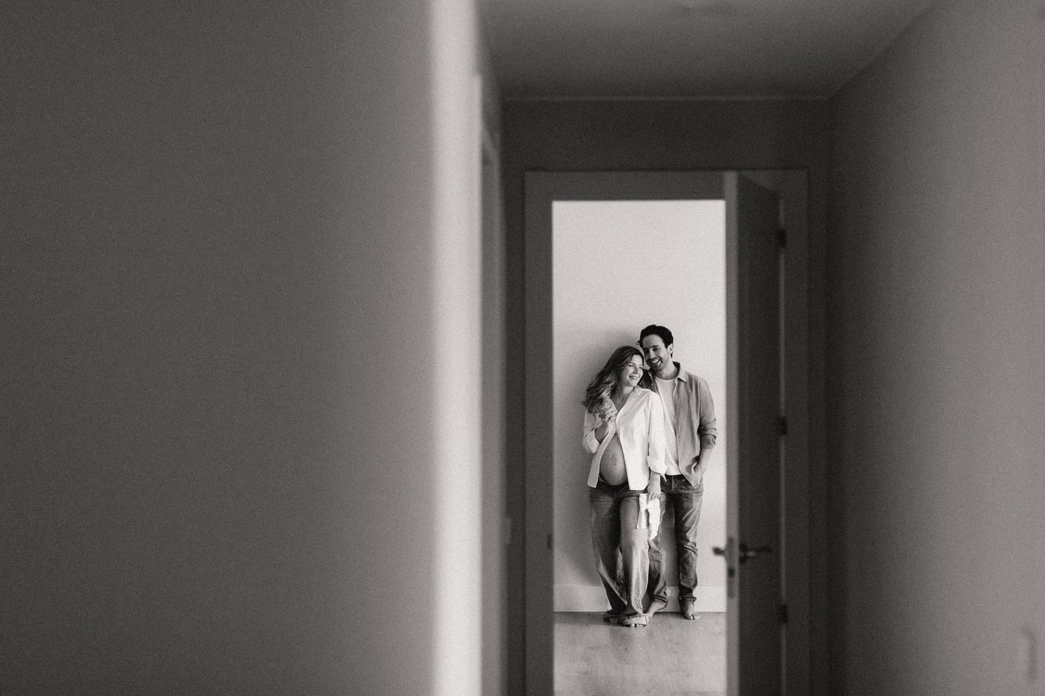 Black and white photo of couple standing together in sunlit hallway doorway of minimalist home.