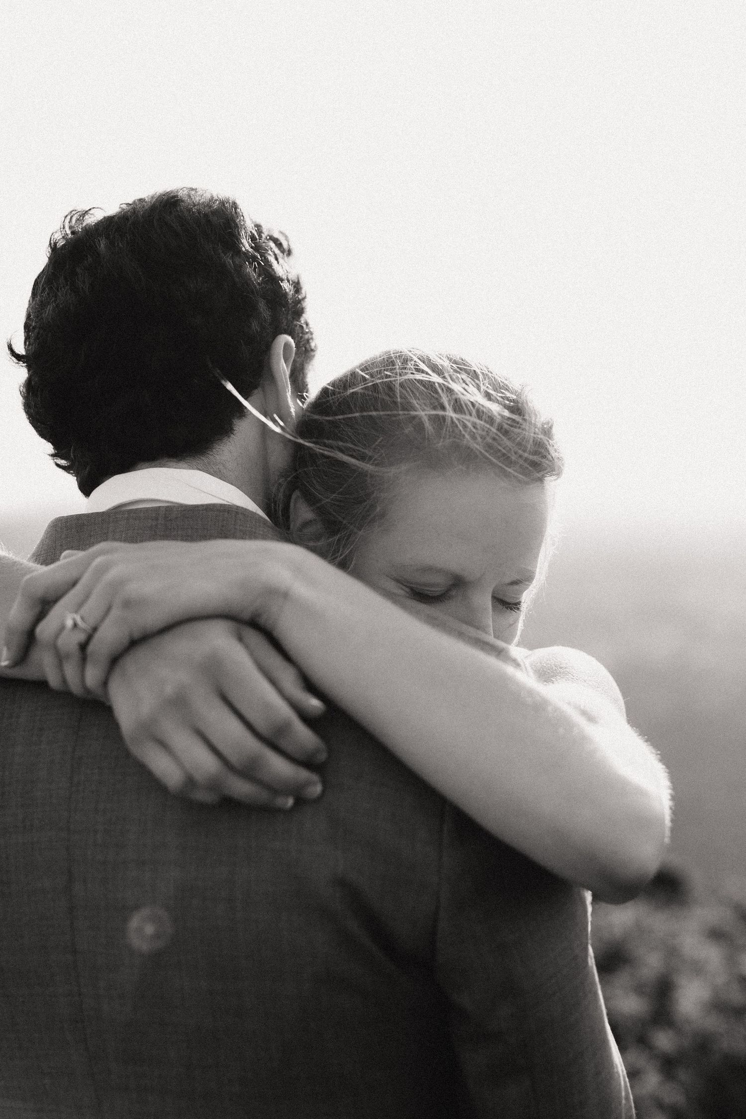 A tender black and white photograph shows a couple embracing outdoors in an intimate moment.
