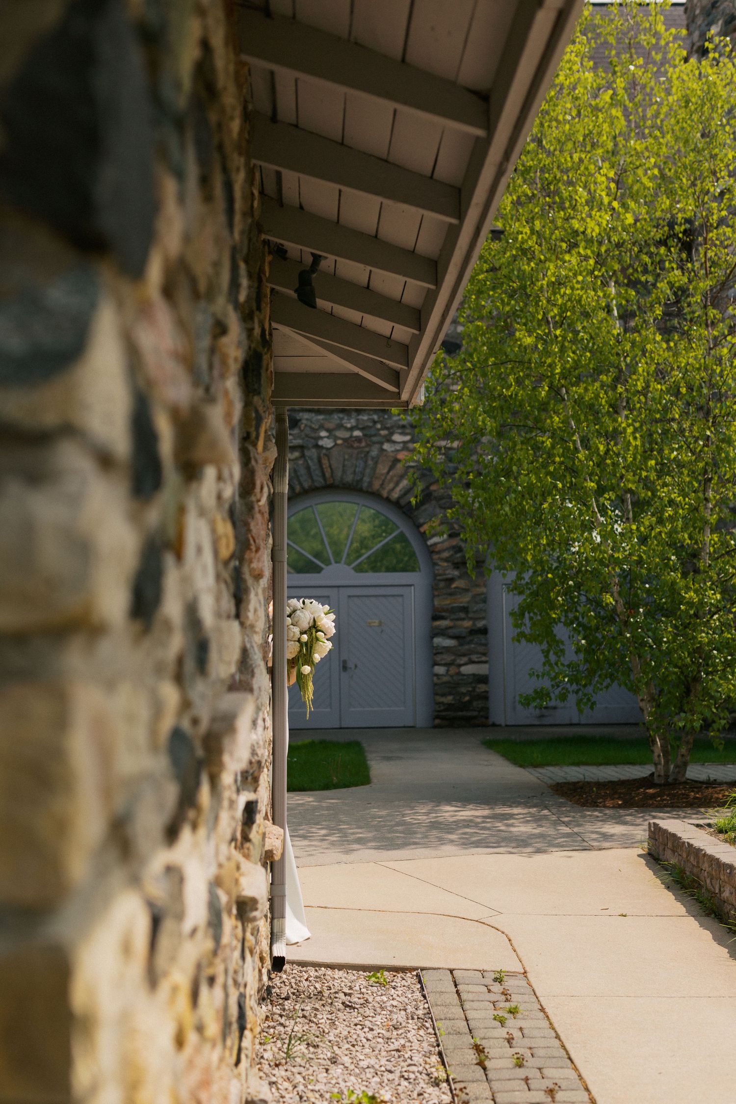 A covered walkway with stone columns leads to a garden path at an outdoor wedding venue.