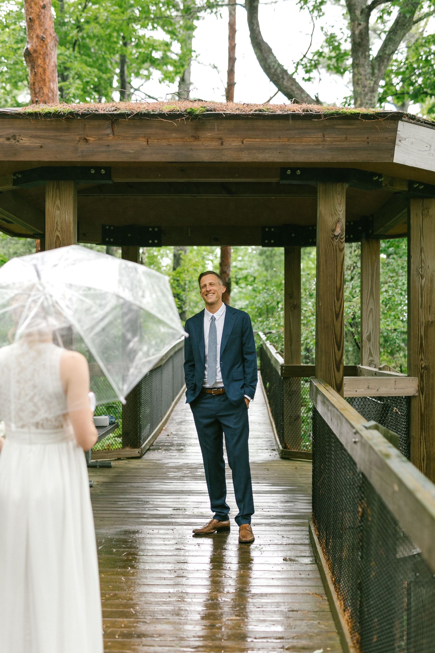 A couple shares a romantic moment on a wet wooden bridge walkway in the forest.