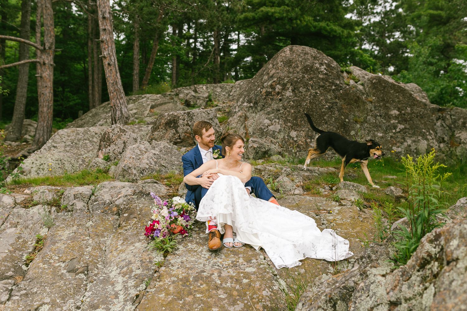 Wedding couple poses on large rocks surrounded by lush green forest.