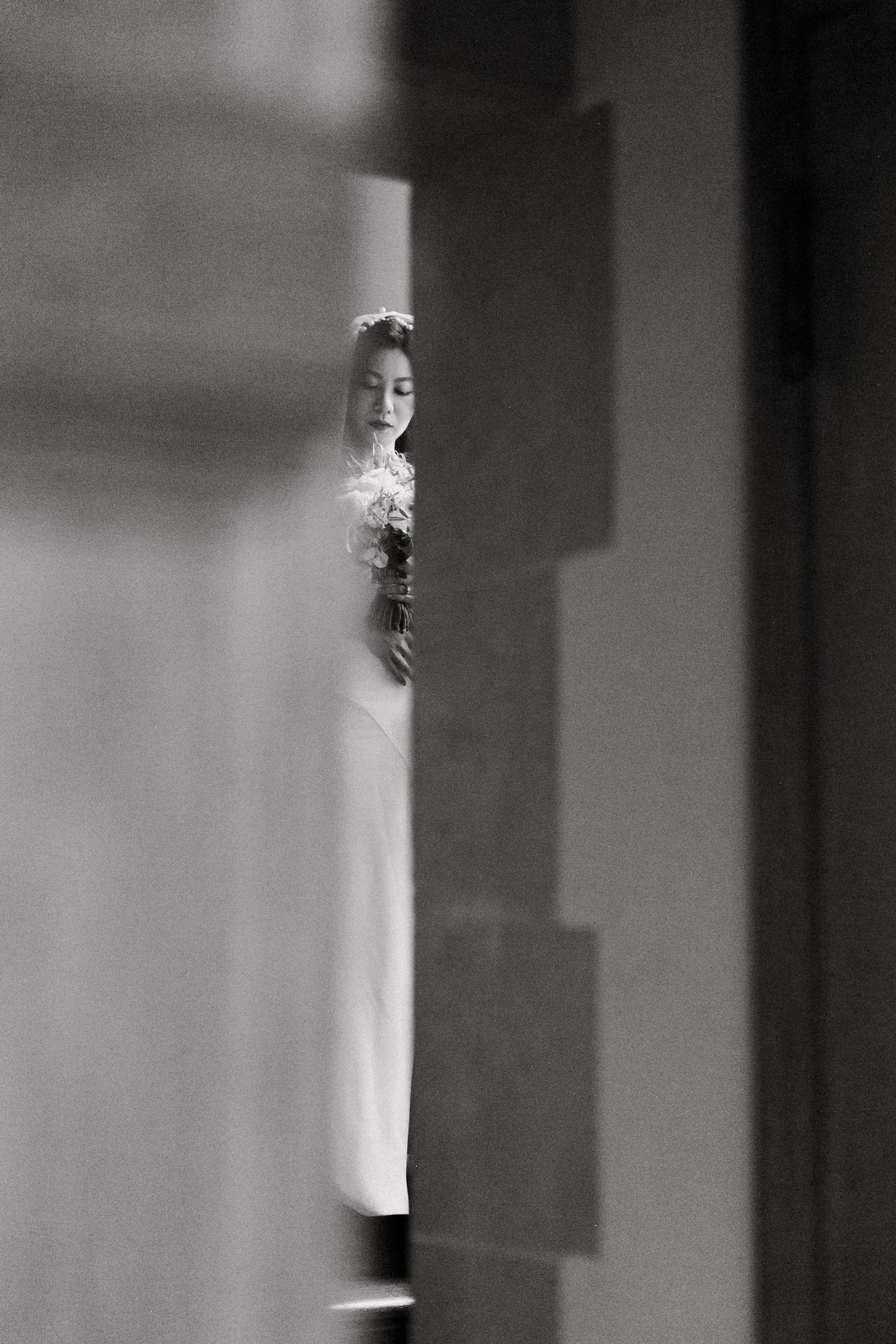Artistic black and white photo of a bride glimpsed through a narrow gap between walls.