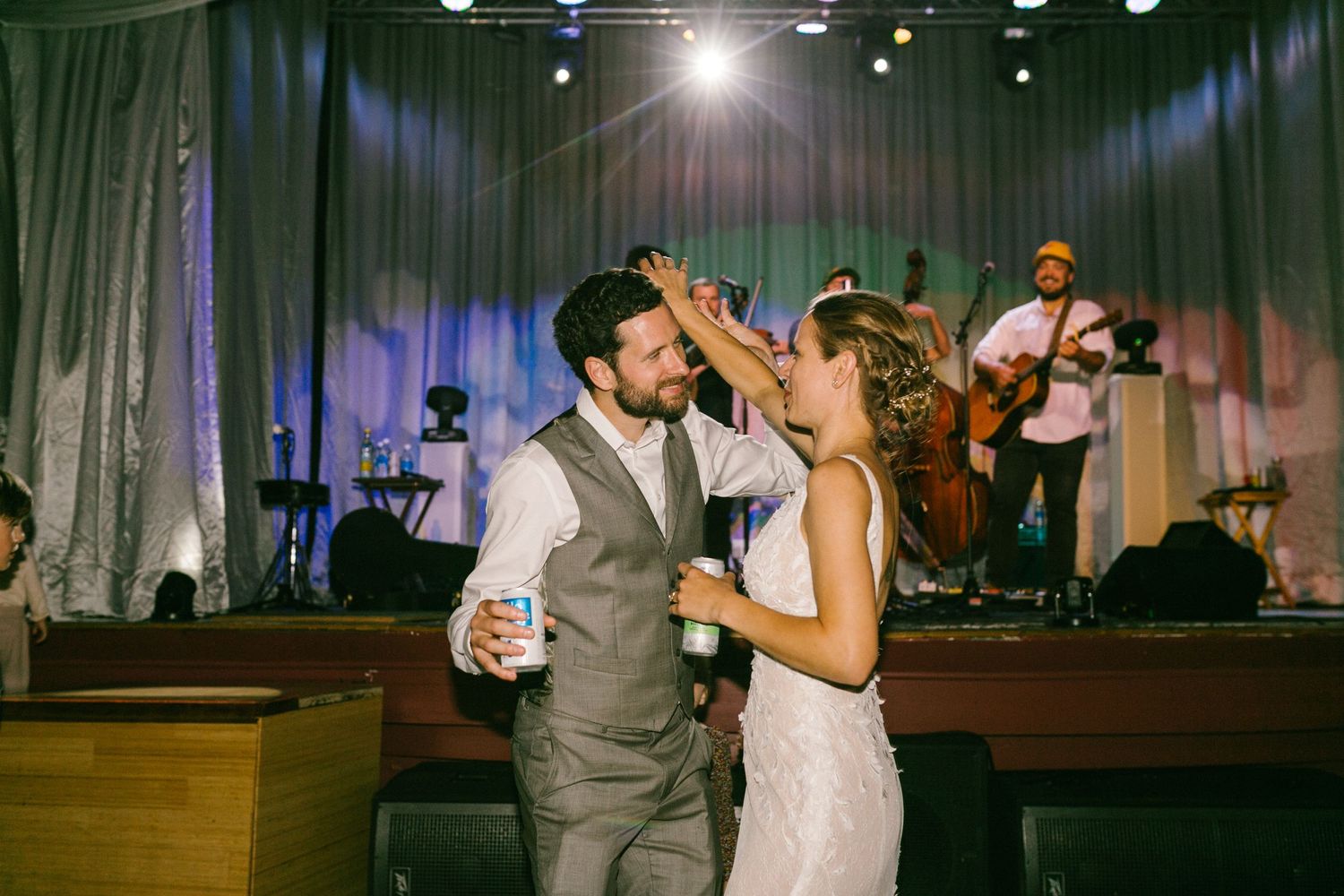A couple shares their first dance at a wedding reception while a band performs on stage in the background.