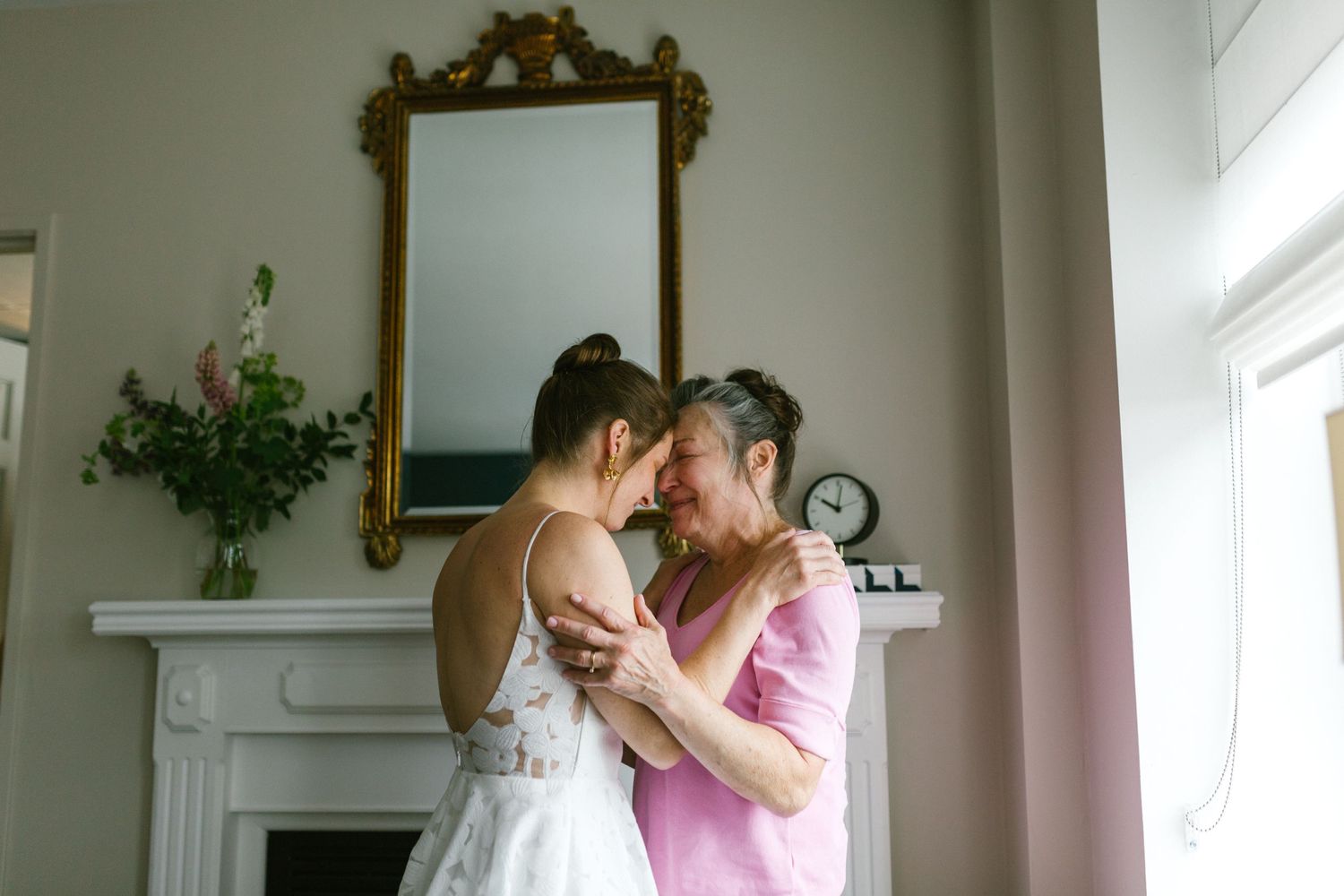 Two people share an intimate moment together in front of an ornate gold mirror and white fireplace mantel.