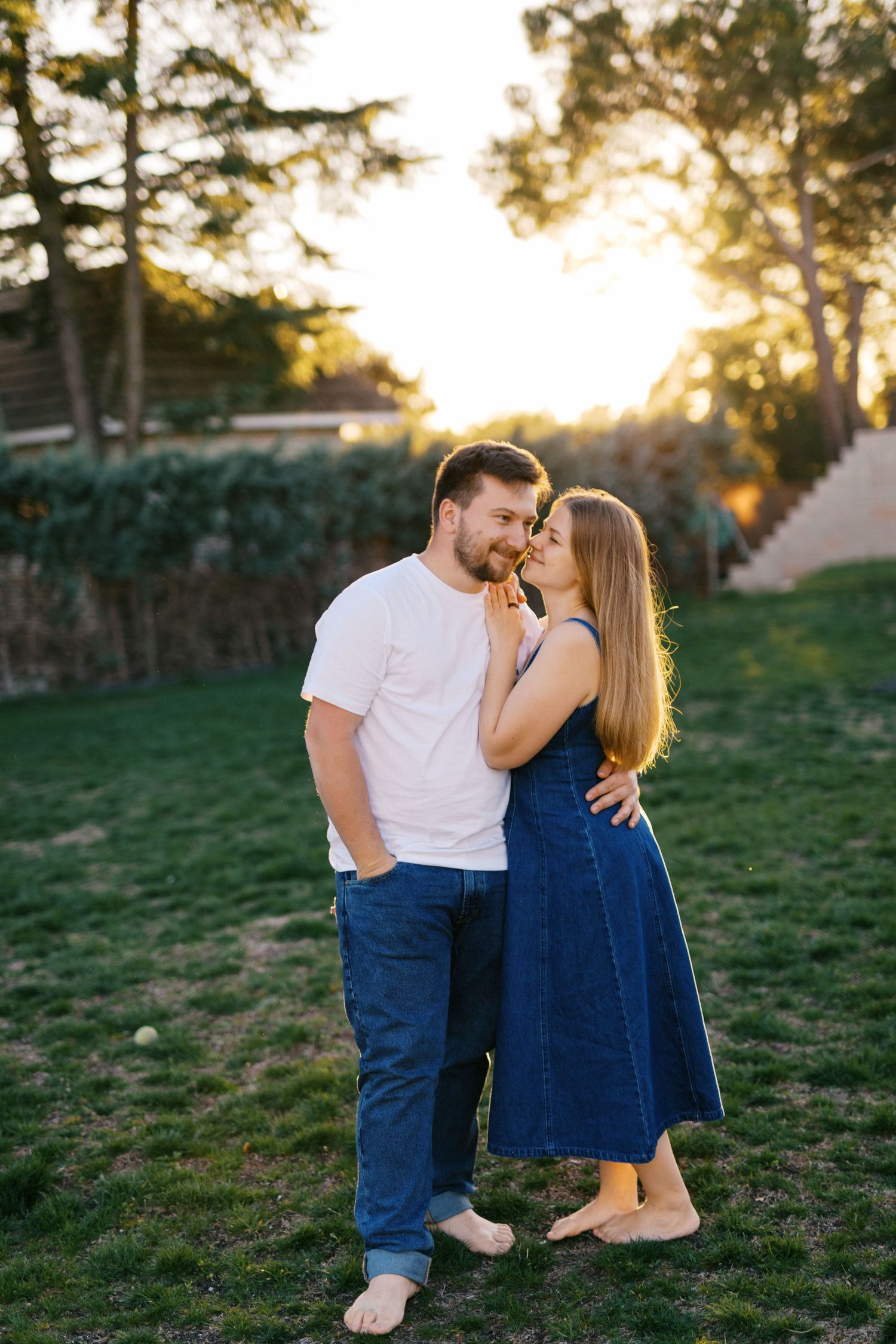 Romantic couple embracing barefoot on green lawn during golden hour sunset in backyard.