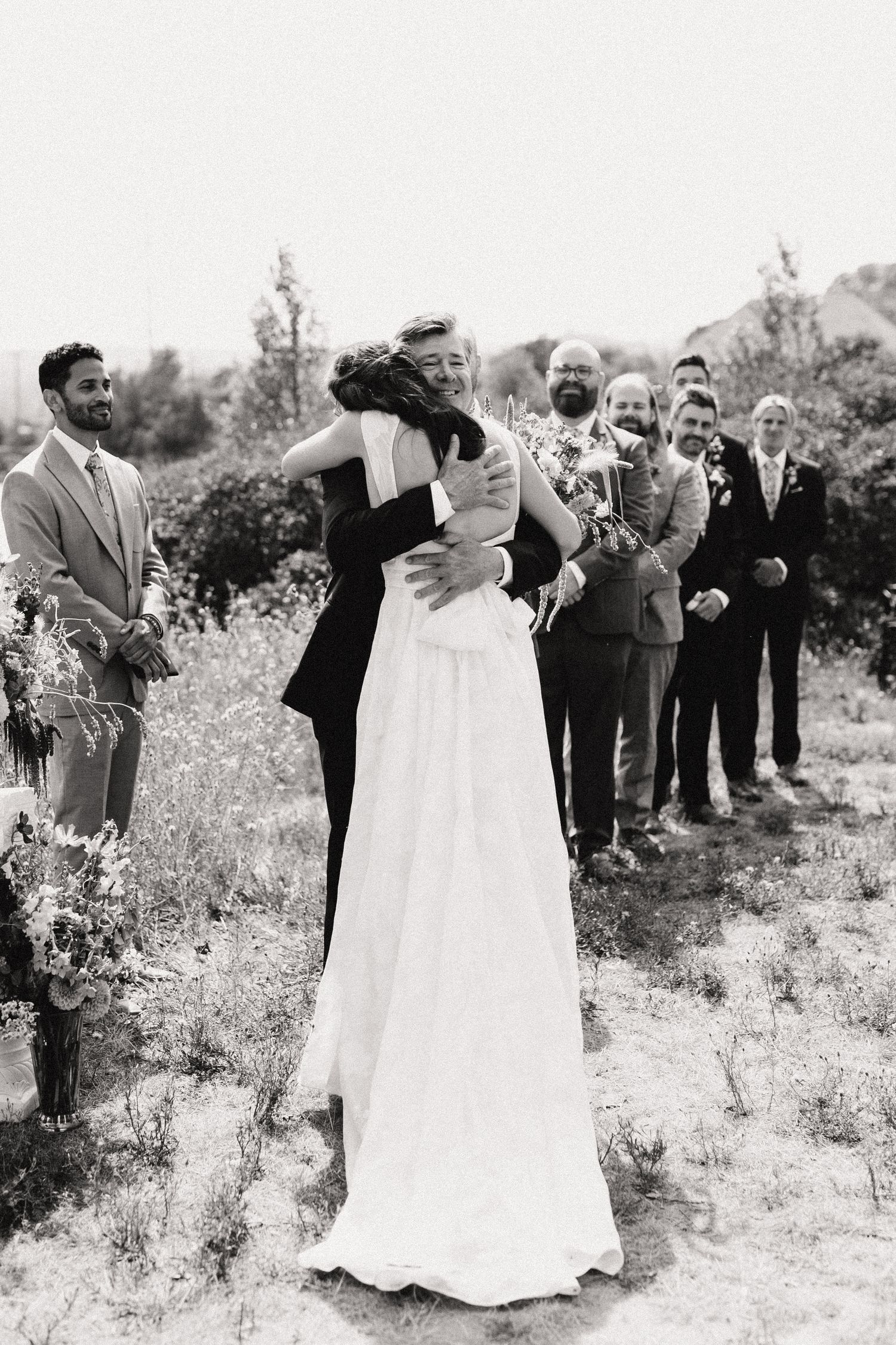 Wedding guests gather in a field of tall grass to celebrate a special moment at an outdoor ceremony.