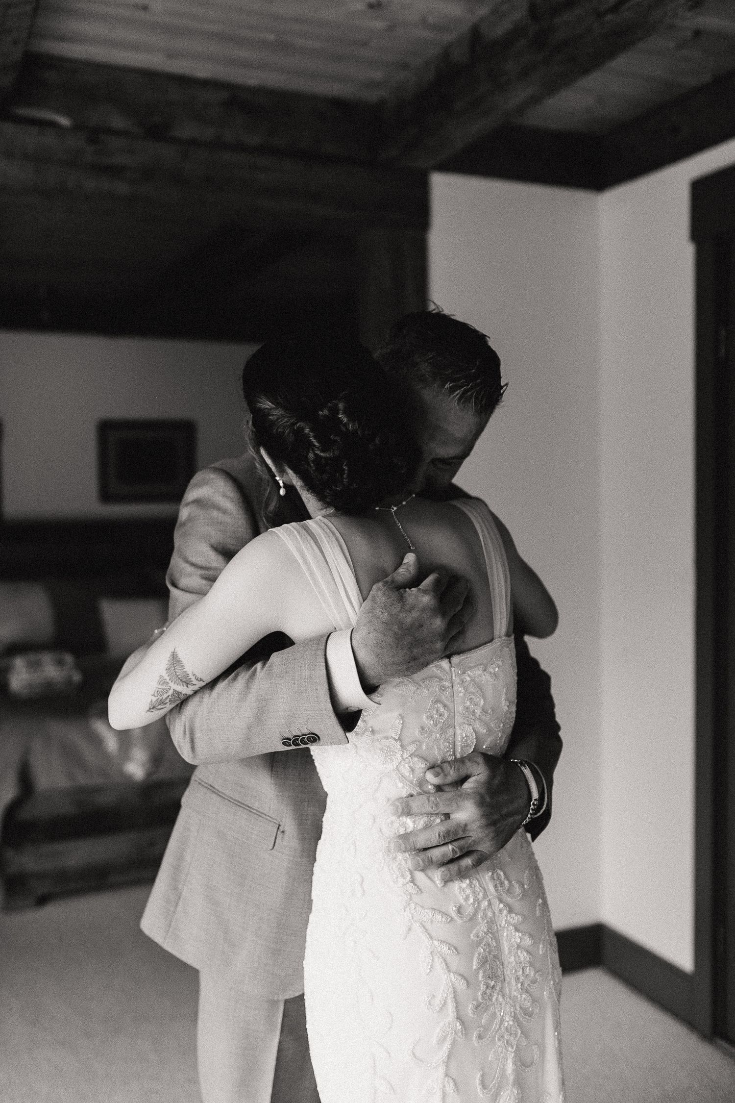 Black and white photo of a bride and her father sharing an emotional embrace on their wedding day indoors.