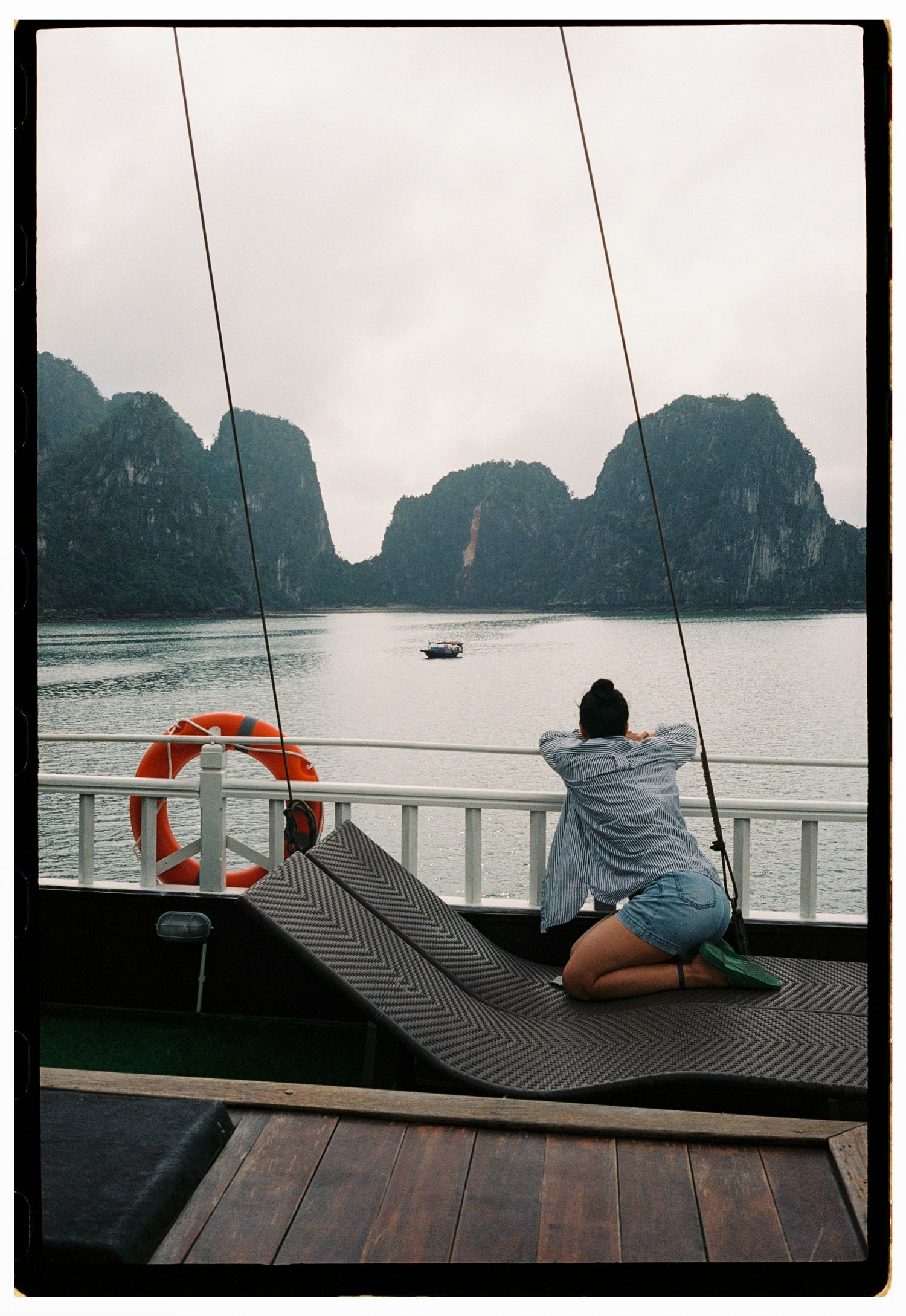 Woman kneeling on deck chair of cruise ship gazing at karst mountains in Ha Long Bay, Vietnam.