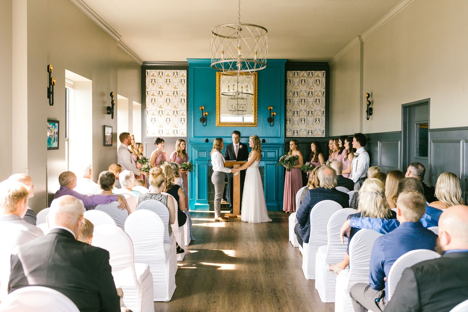 Audience members seated in rows watch a presentation in a room with turquoise walls and white trim.