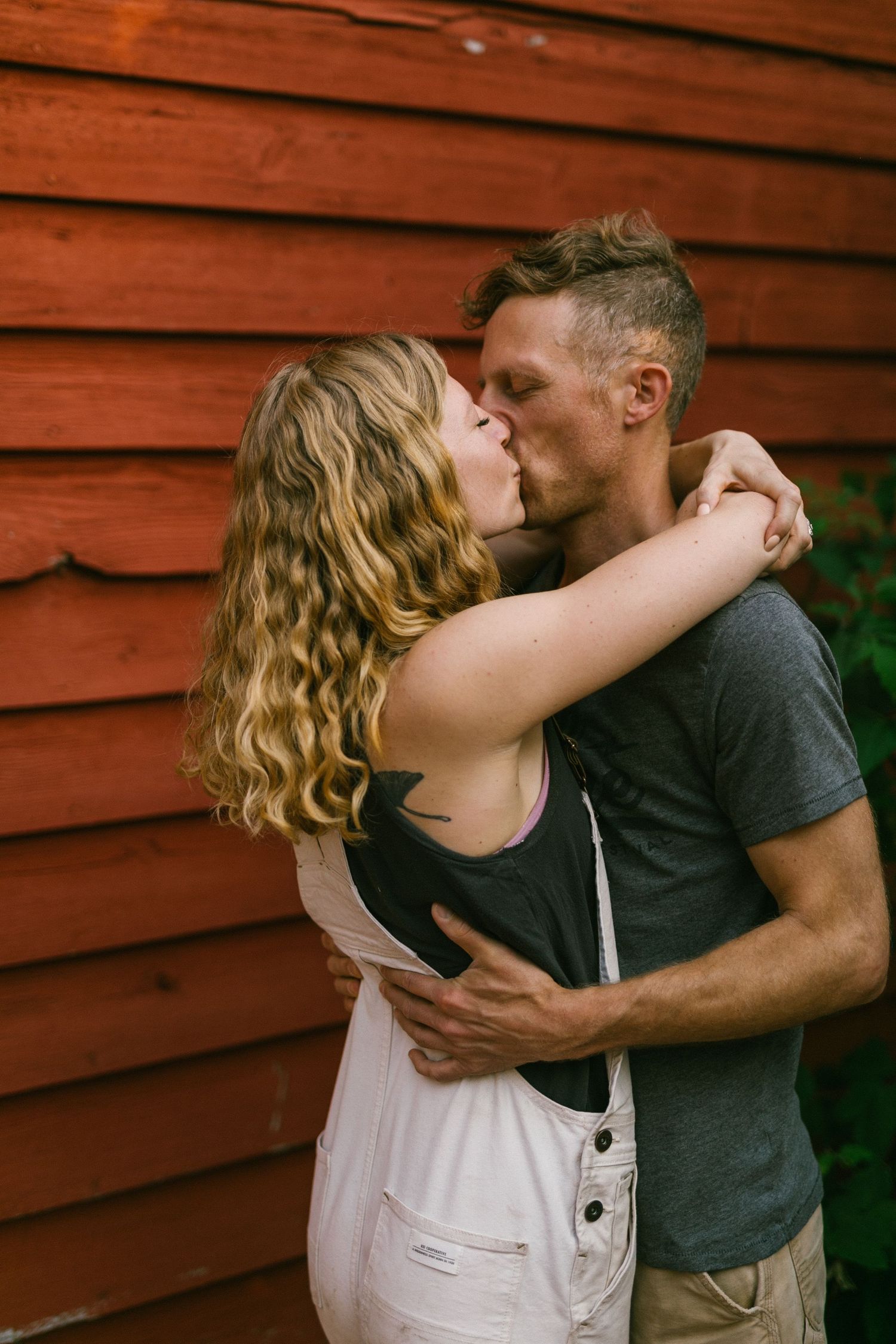 Romantic embrace against weathered red barn siding in warm evening light.