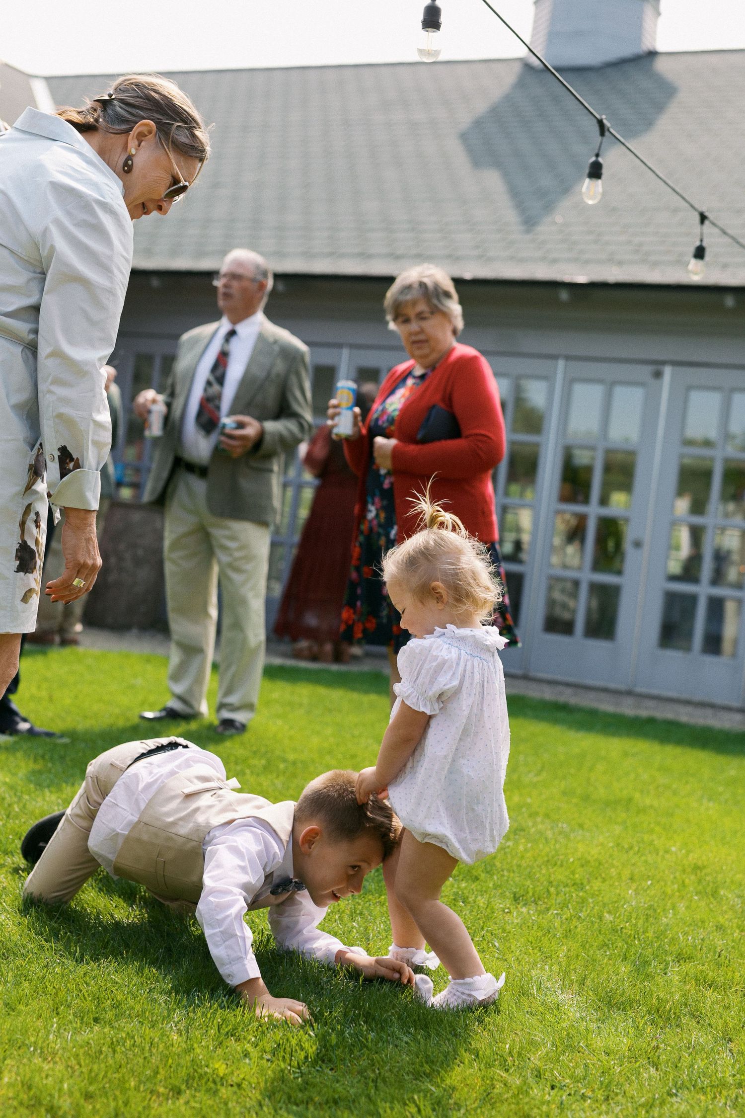 Series of playful children falling and playing on green grass during an outdoor event near a white building.