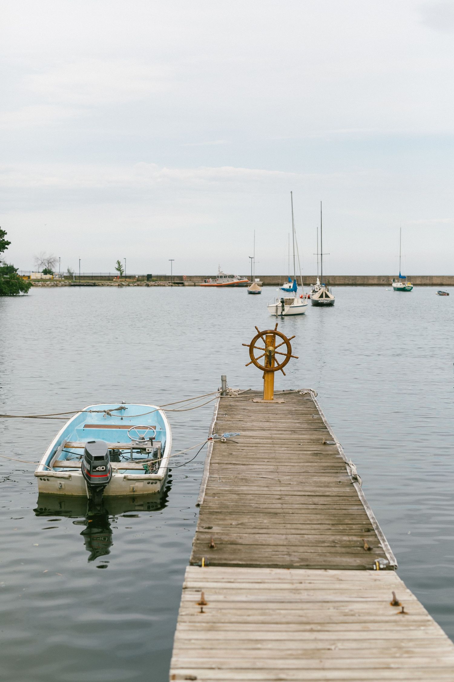 Small boats are moored alongside a weathered wooden pier extending into a peaceful harbor.