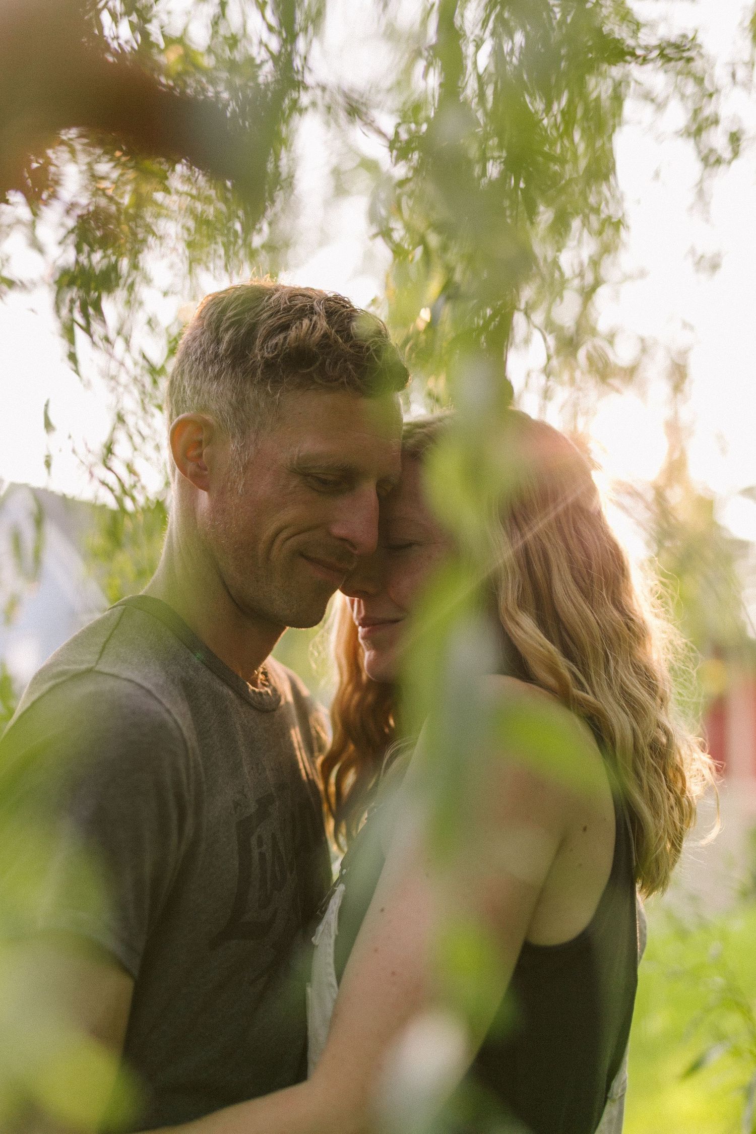 A romantic couple shares an intimate moment in soft natural lighting through green foliage.