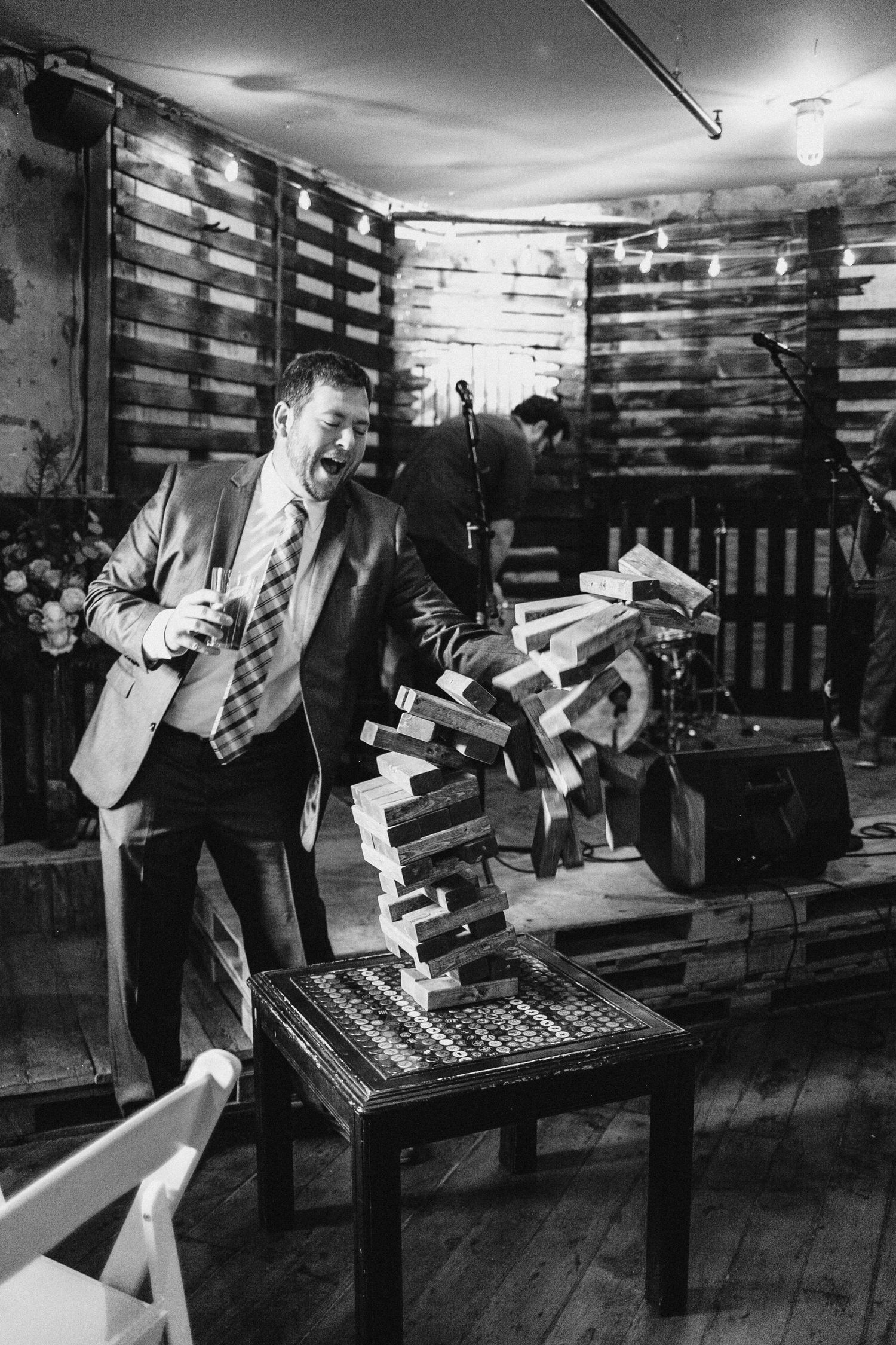 Vintage black and white photo of a wedding guest crashing a giant jenga game during wedding reception.