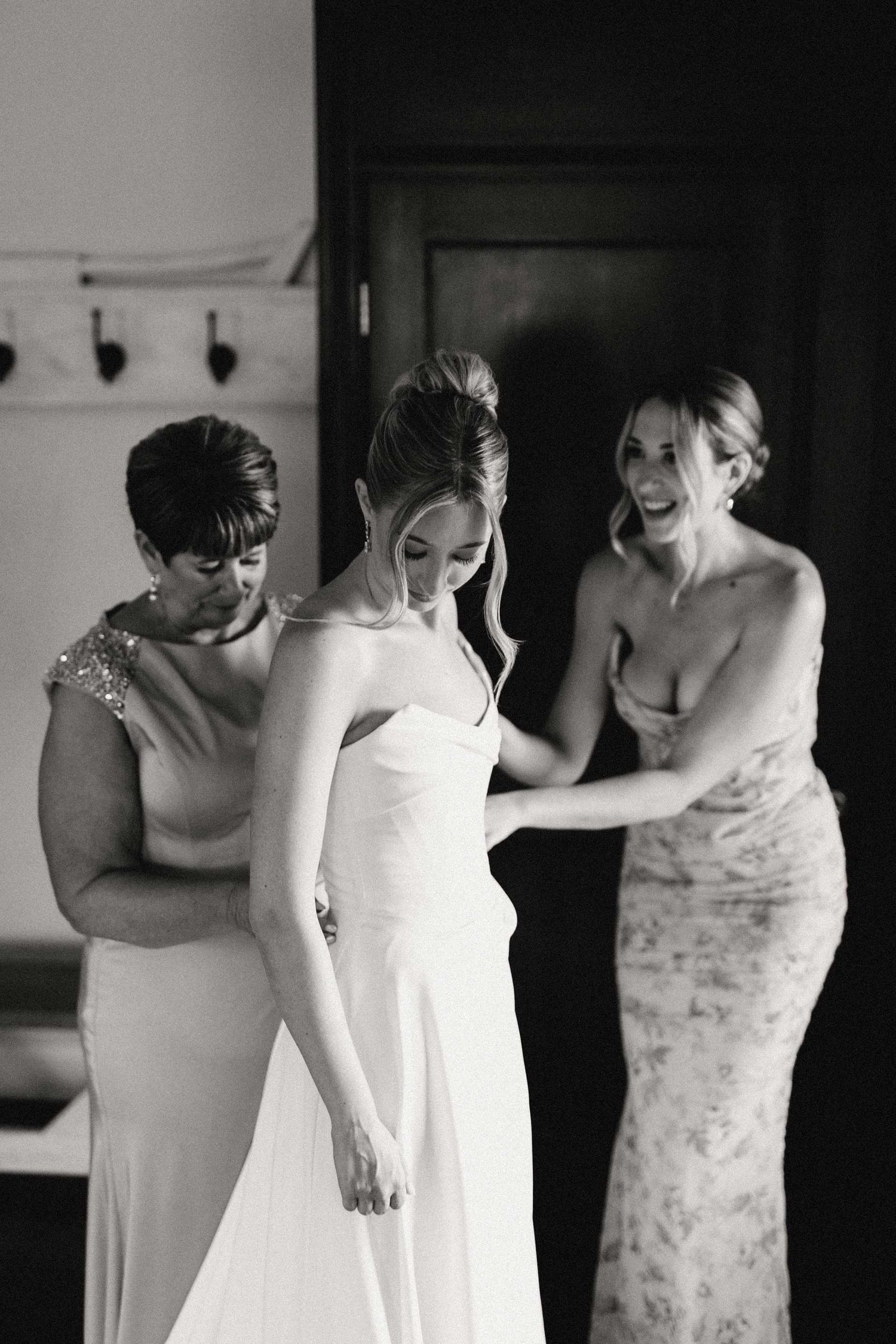 Black and white sequence showing a bride and her mother and sister make final adjustments of the wedding dress during preparation.