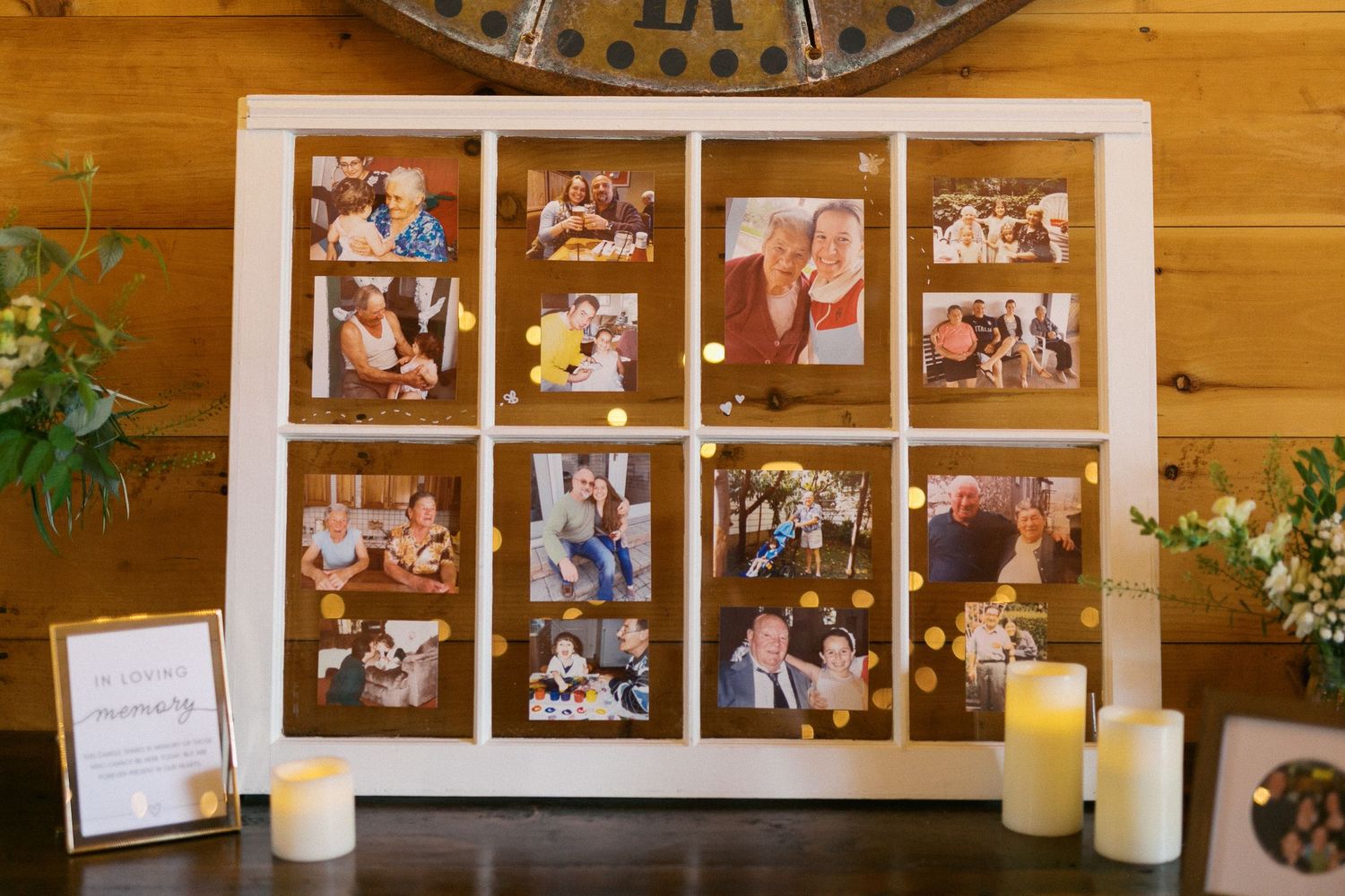 Vintage window frame displaying commemorative photos with gold dot accents, flanked by white candles on a rustic wooden table.