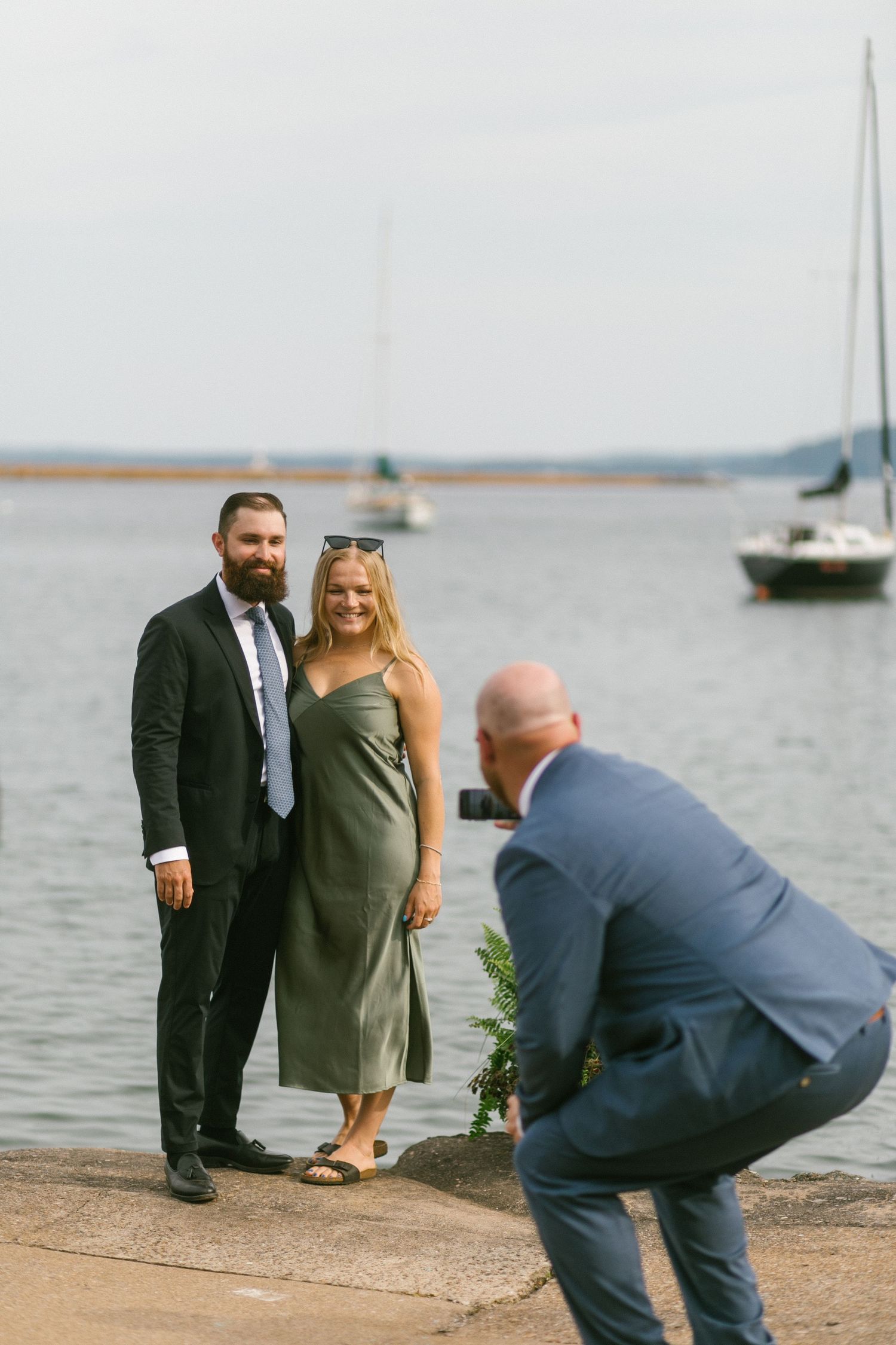 A couple poses for photos by the waterfront while a photographer captures their special moment.