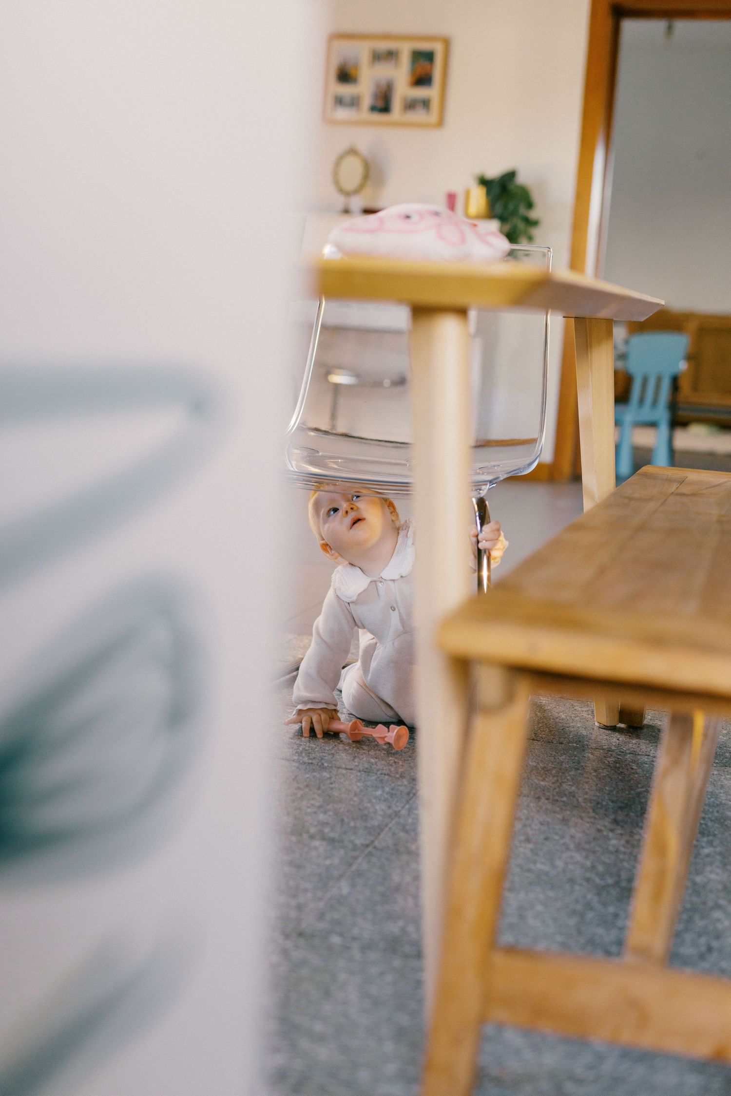 Curious baby sitting on floor looking up while exploring under wooden furniture indoors.