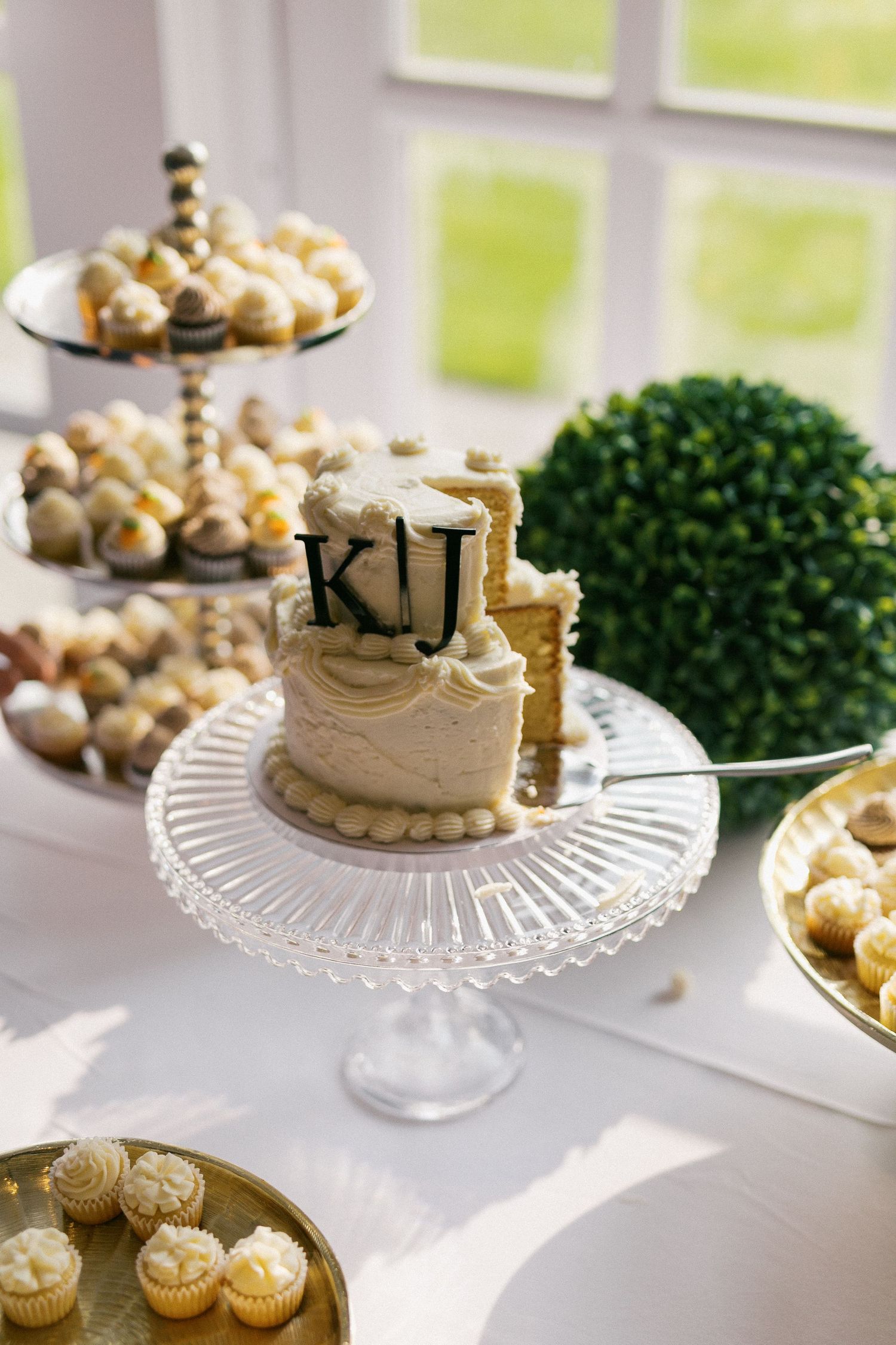 Elegant dessert display featuring white cakes and treats on crystal cake stands at a wedding reception.