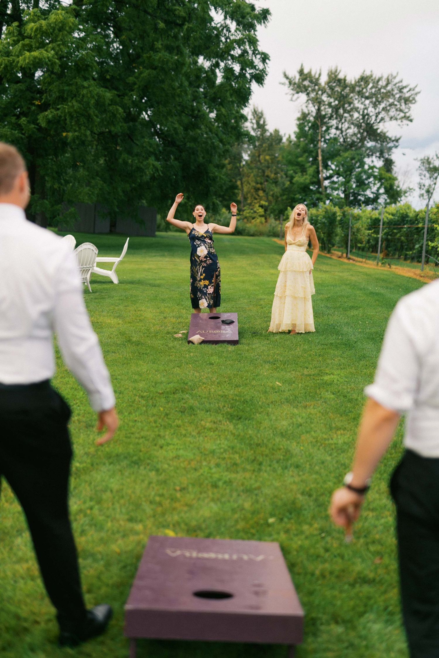 People playing cornhole lawn game at an outdoor event with green grass and trees in the background.