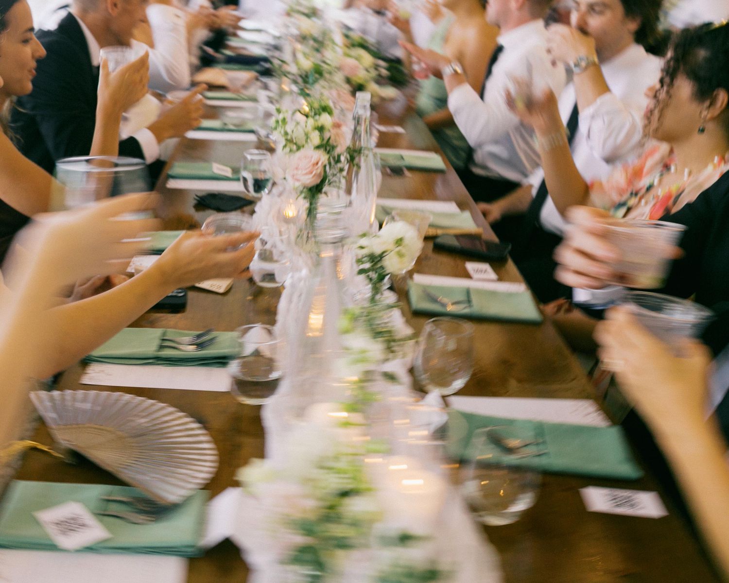 Elegant table setting at a dinner party with candlelight, floral centerpieces and guests seated along both sides.