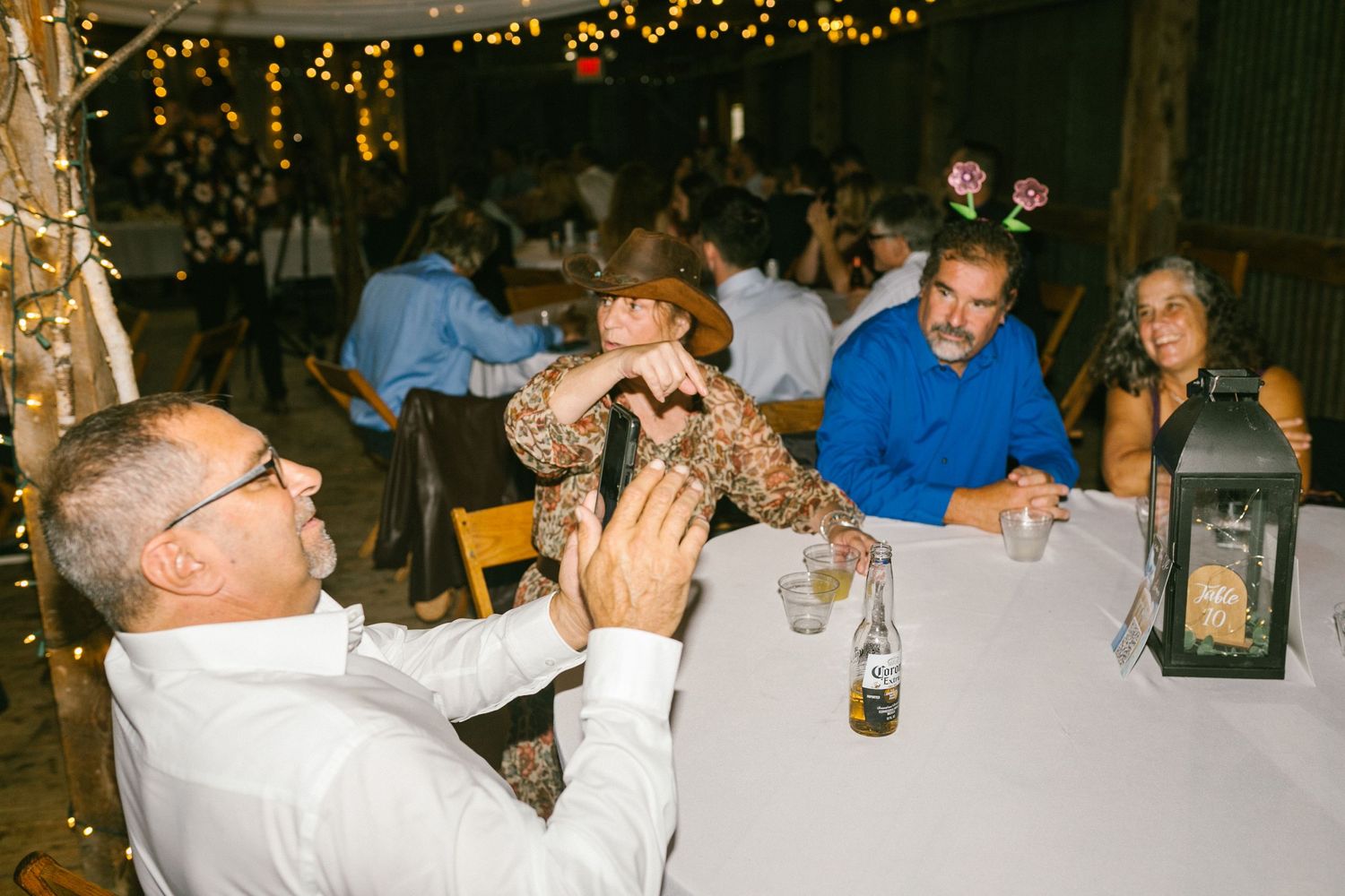 People gathered at tables for an evening wedding reception with string lights and lantern decorations.