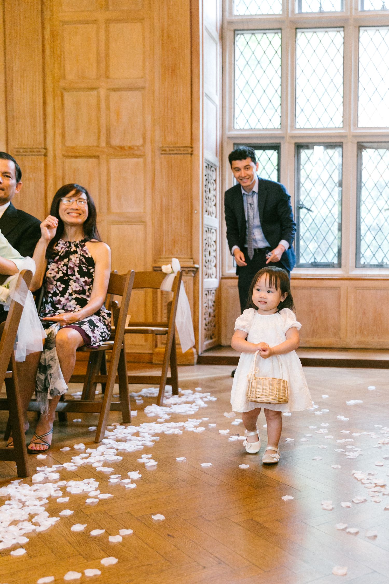 Adorable flower girl walking down the aisle scattering white petals at a wedding ceremony.