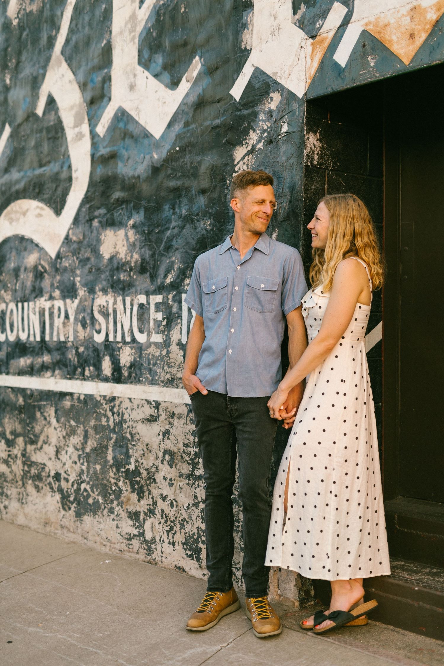 Couple standing together against a rustic wall with vintage text and graphics.