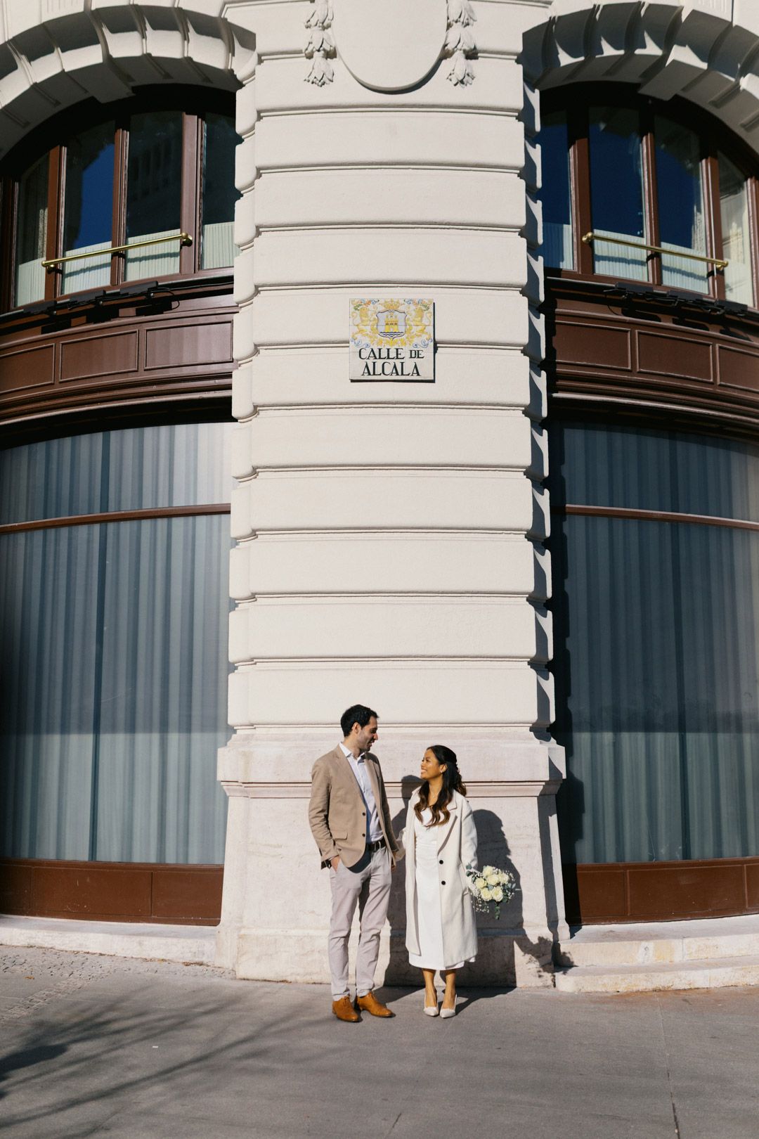 Couple sharing a romantic moment on a sunny street corner below a Calle de Alcala sign in Madrid.