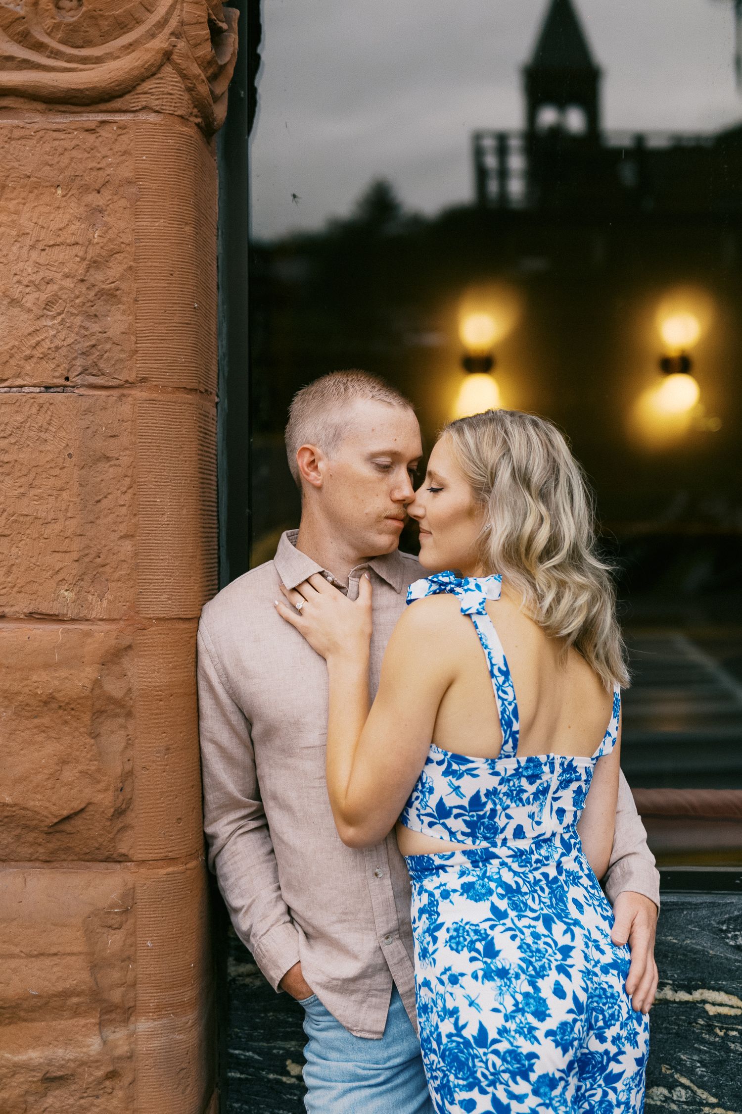 Couple sharing a romantic kiss against a stone wall with warm bokeh lights at dusk.