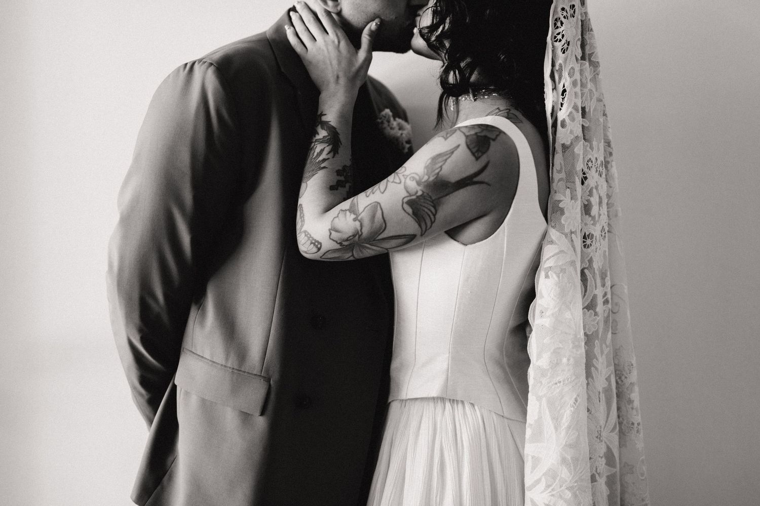 Black and white photo of a tattooed bride and suited groom sharing an intimate kiss.