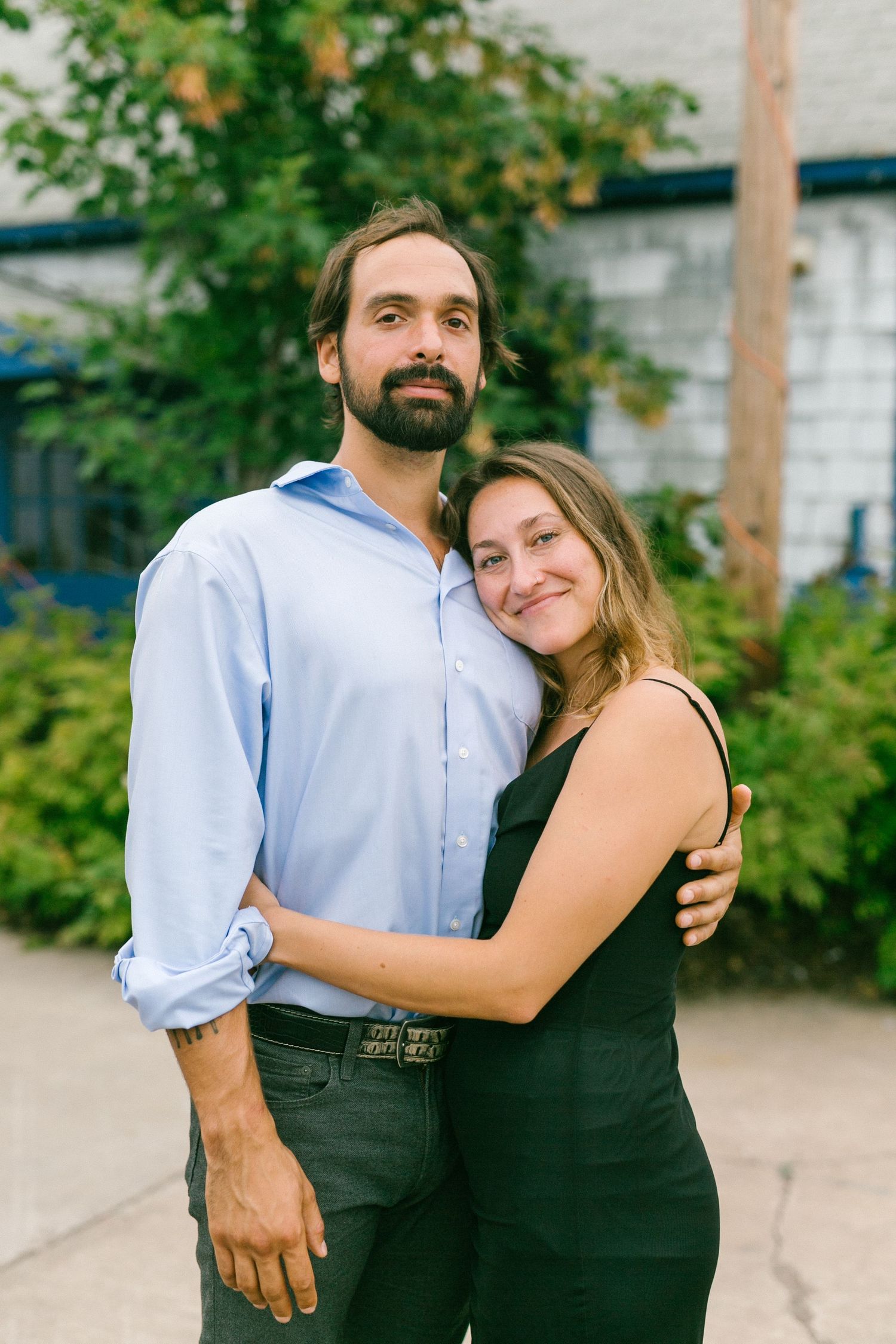 A couple embracing outdoors against a green leafy background on a sunny day.