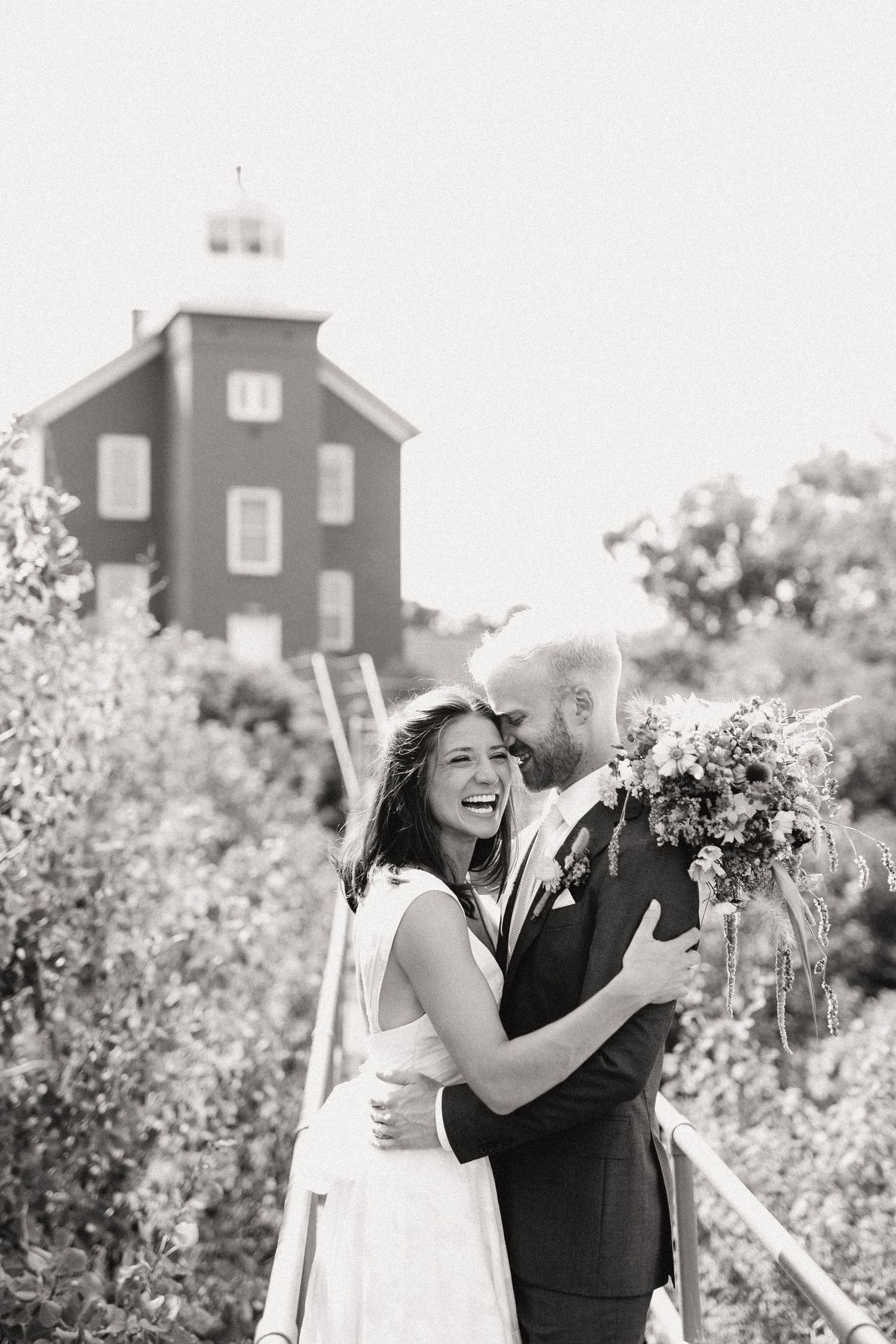 A joyful wedding moment captured in black and white with a red building in the background.
