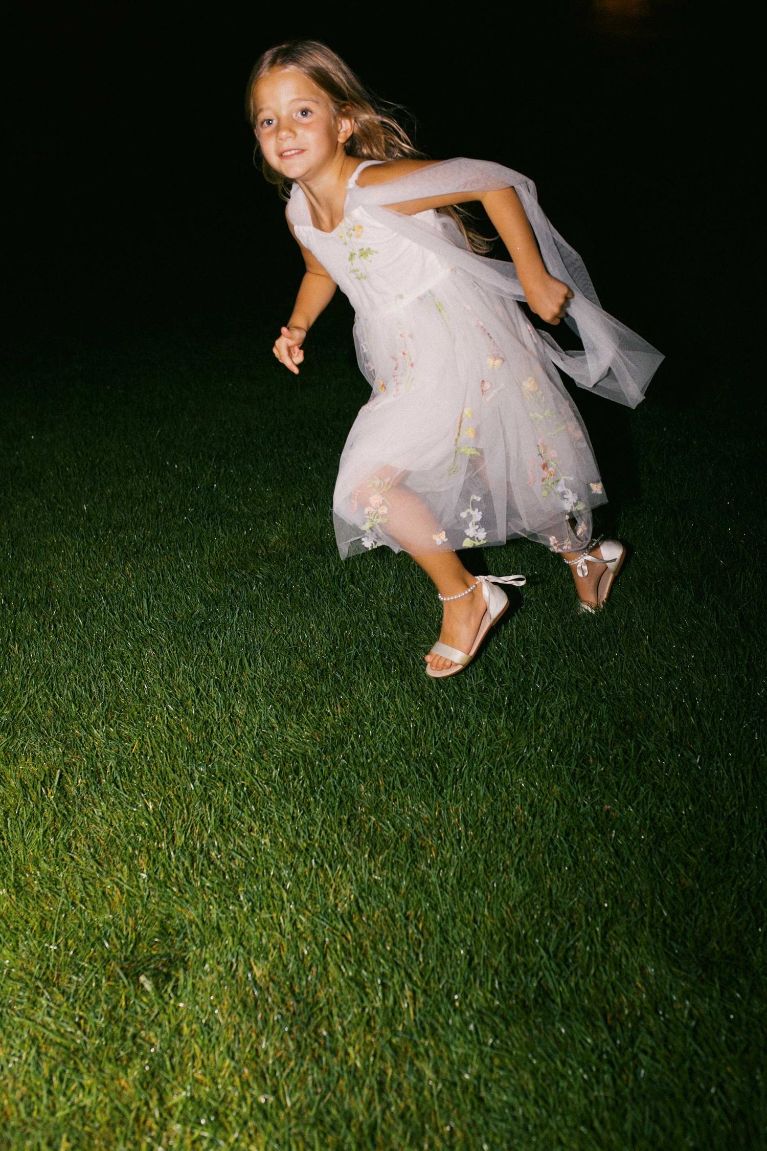 A young girl in a flowing white dress runs on a dark green lawn at night.