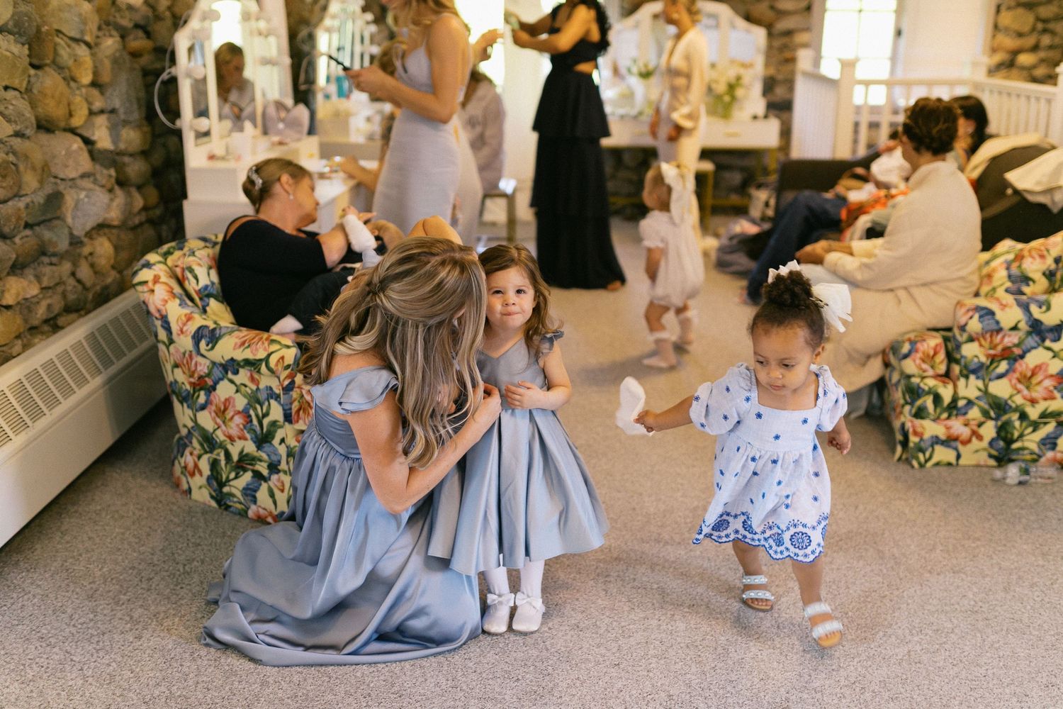Wedding party in light blue dresses gathered in a rustic stone-walled venue.