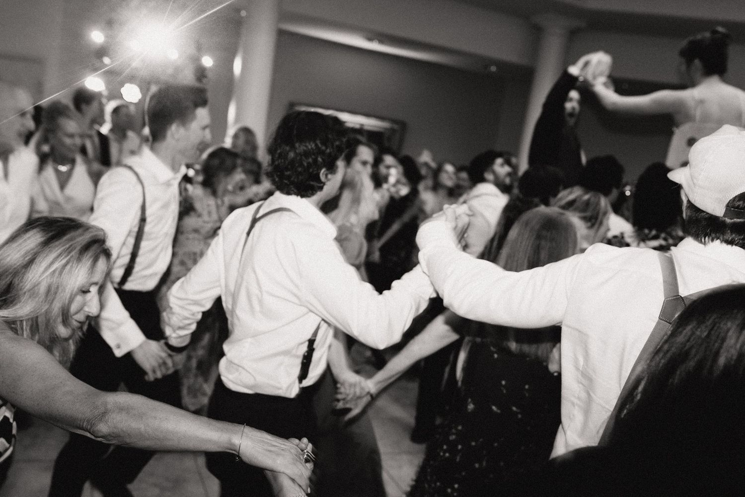 Black and white photo of wedding guests dancing and celebrating in formal attire.