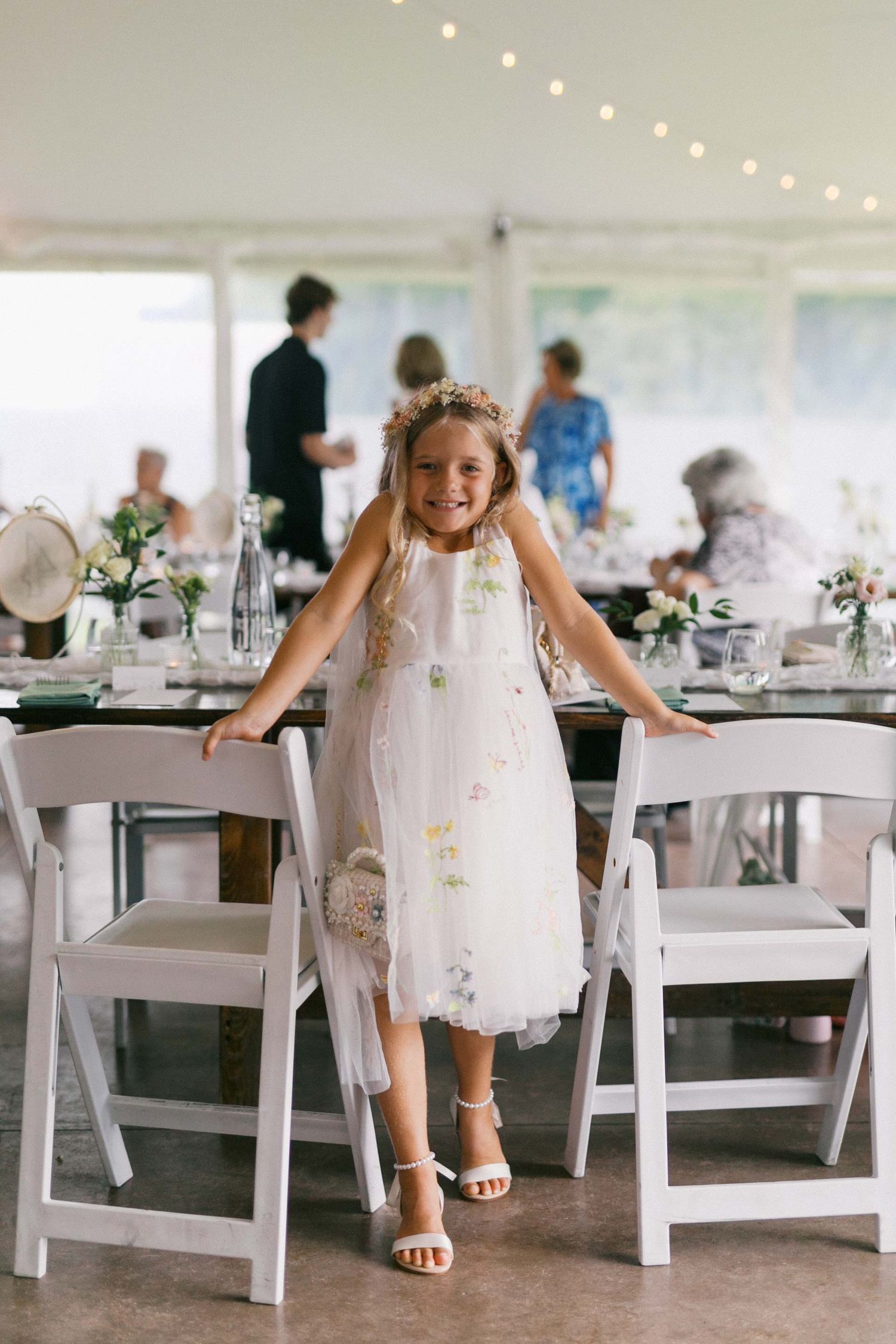 A white reception tent decorated with string lights and folding chairs set up for an elegant wedding celebration.