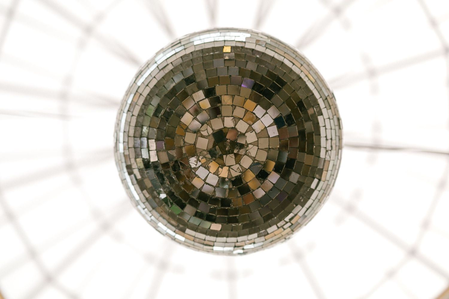 Looking up at a circular disco ball with mosaic mirror tiles reflecting light in a radial pattern.