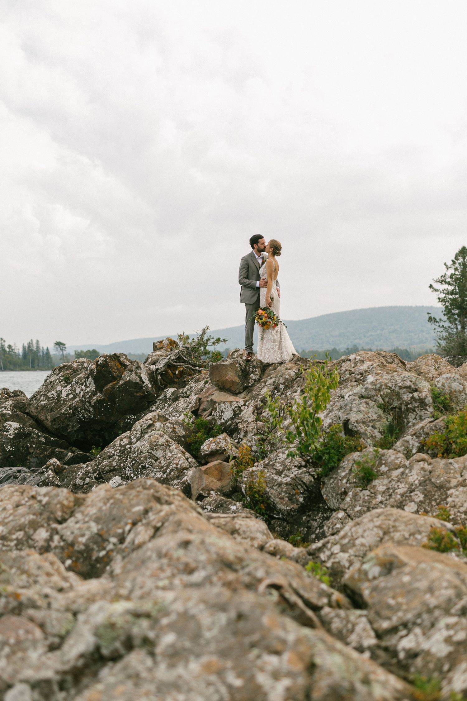 A couple shares a romantic moment while standing on rocky terrain with misty mountains in the background.