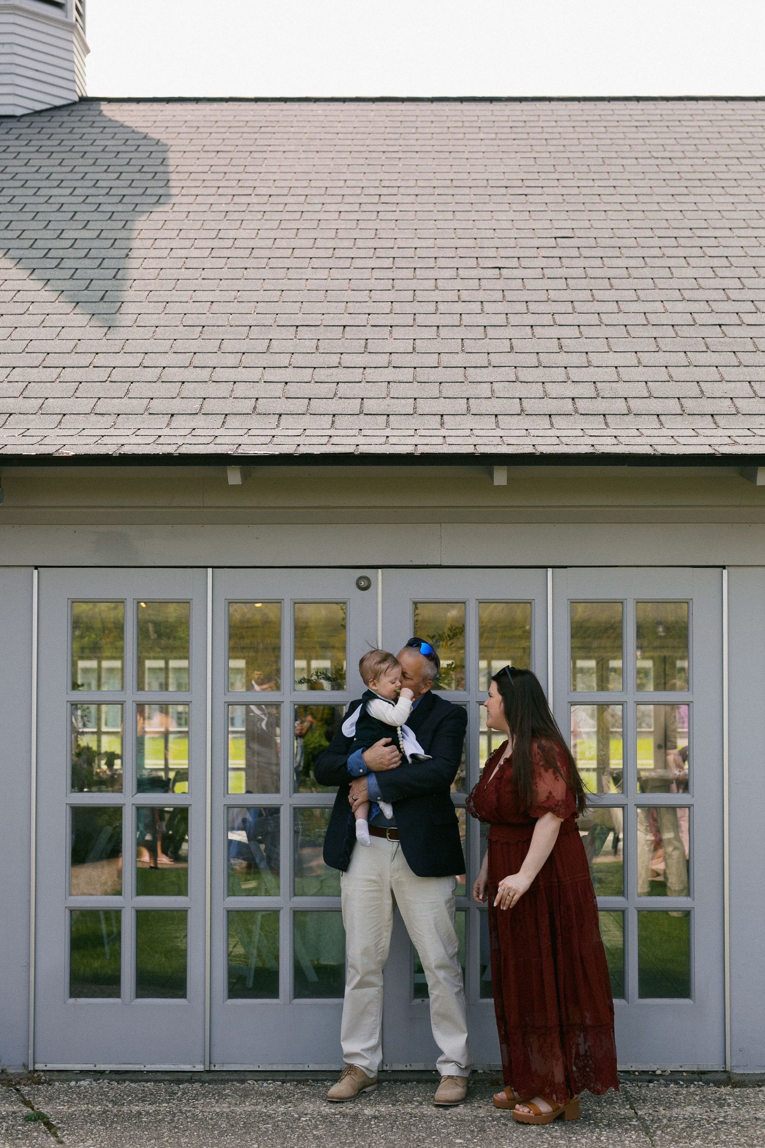 Wedding party posing against white building exterior with paneled windows and brick detailing.