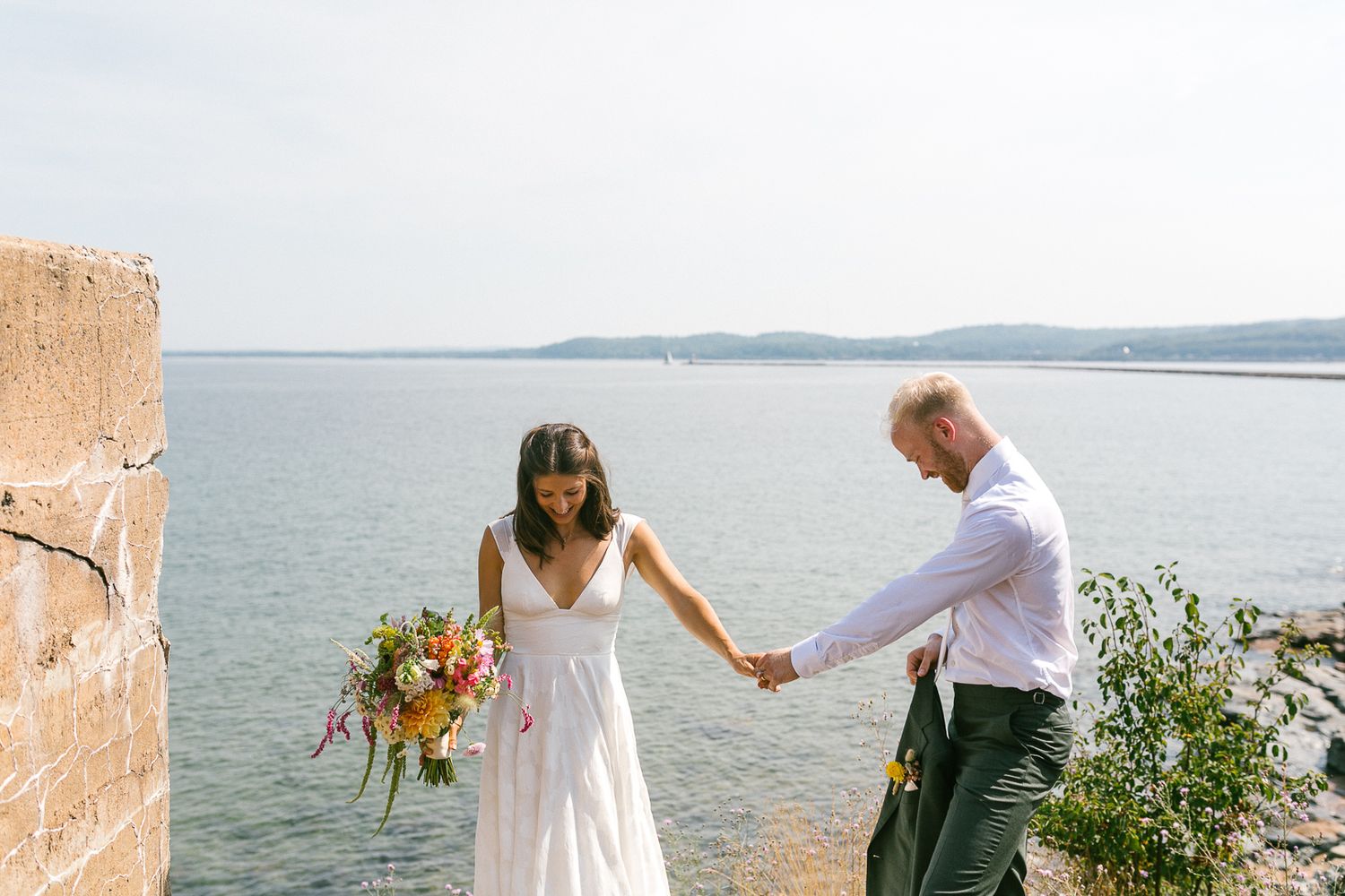 A romantic seaside wedding ceremony with boats visible in the harbor background.