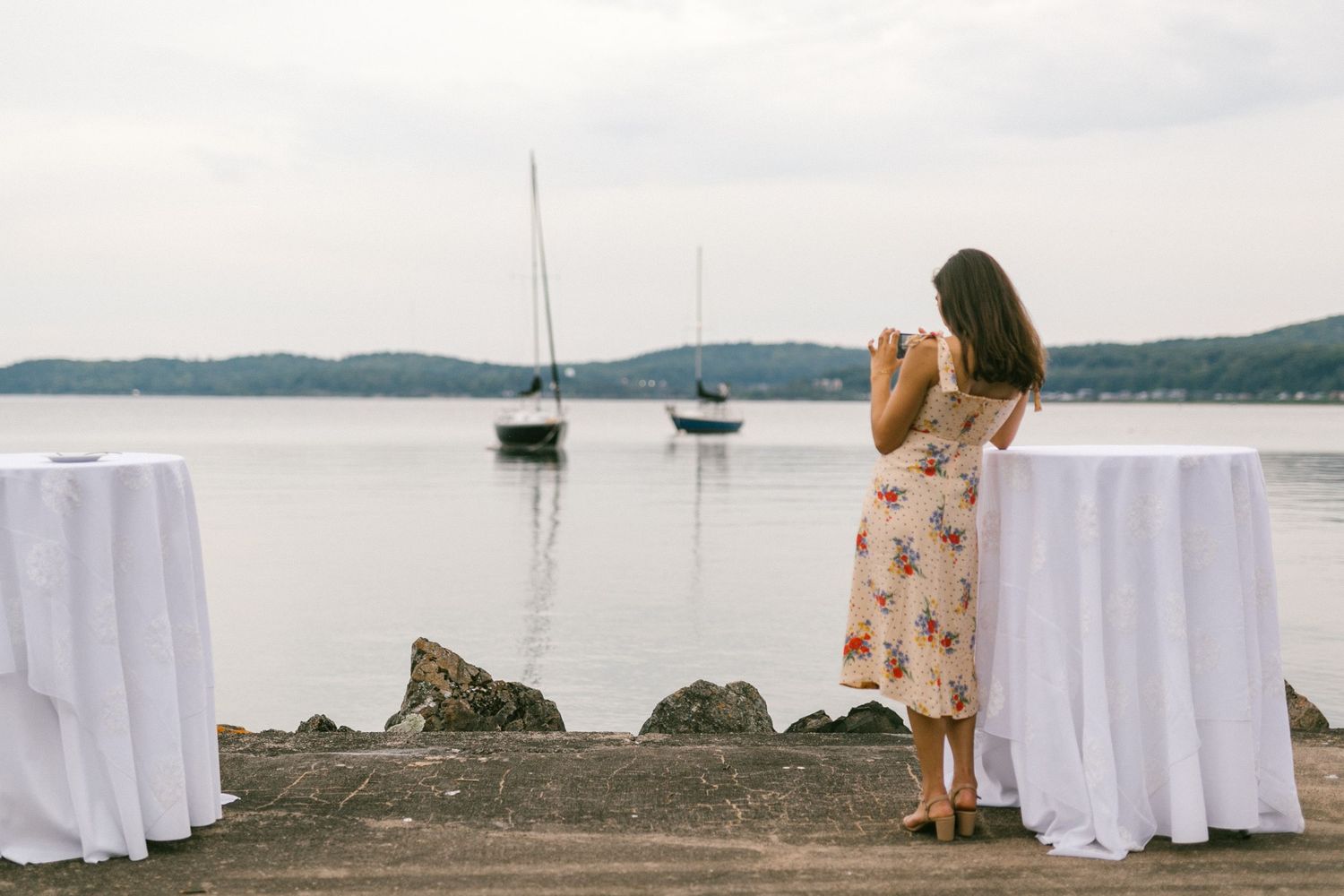 White-clothed tables set up for an outdoor event with boats visible in the harbor.