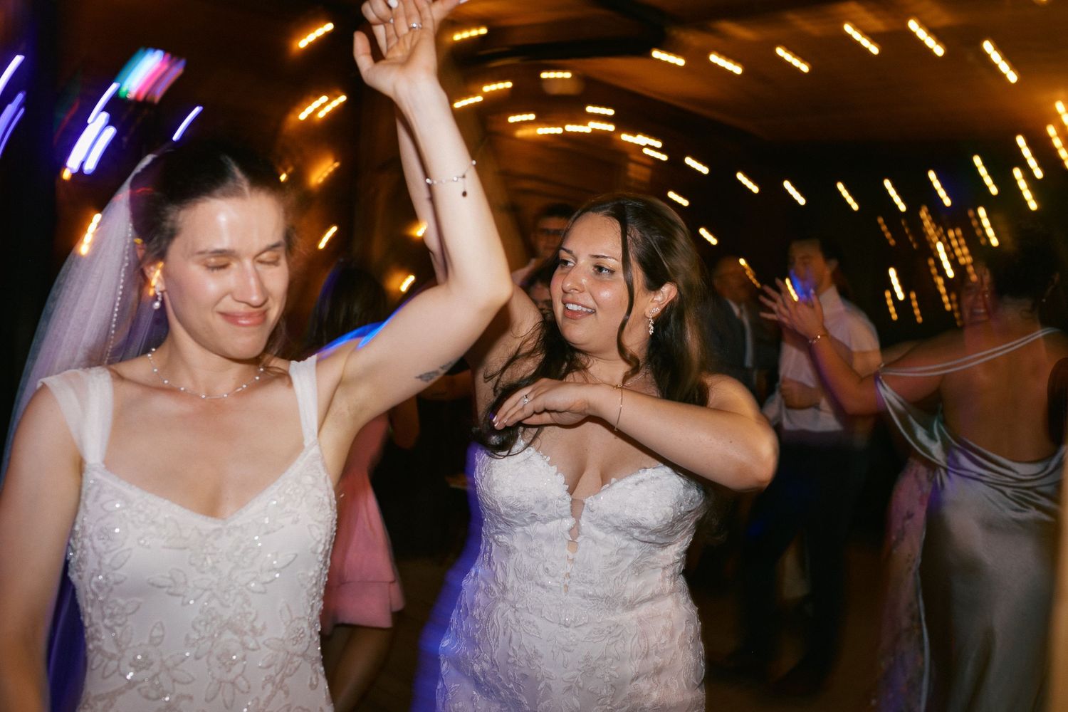 Two brides in white wedding gowns dancing joyfully together at their wedding reception.