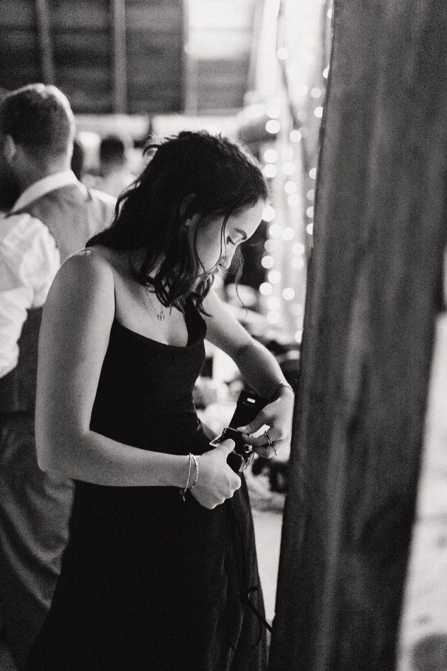 Black and white photo of person in formal dress changing film in a film camera at a wedding reception.