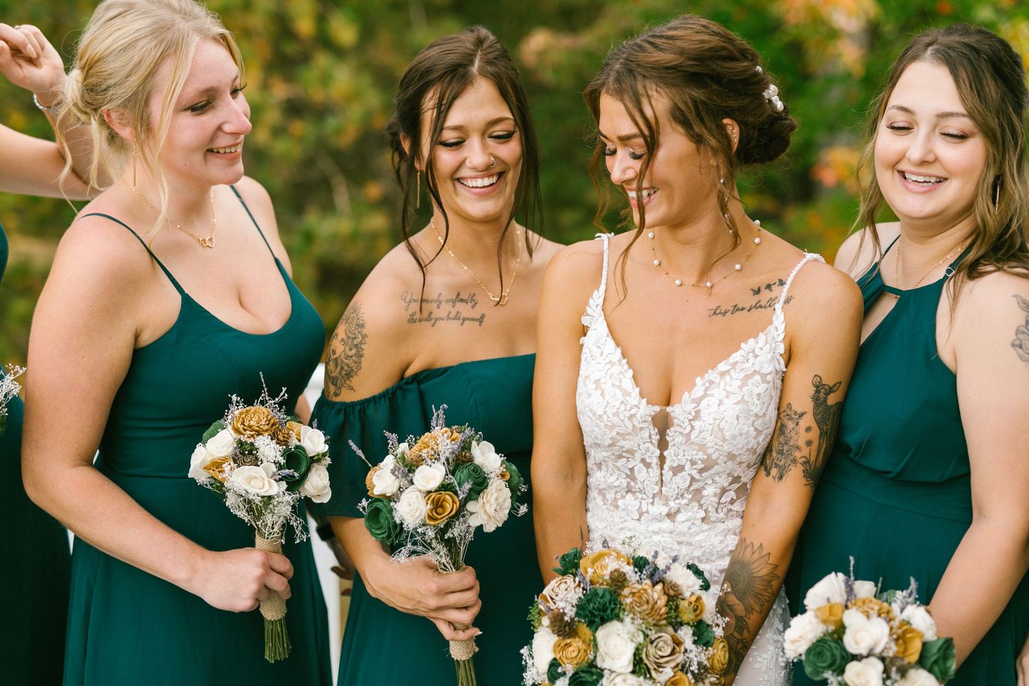 A wedding party wearing emerald green dresses and holding white floral bouquets share a candid moment outdoors.