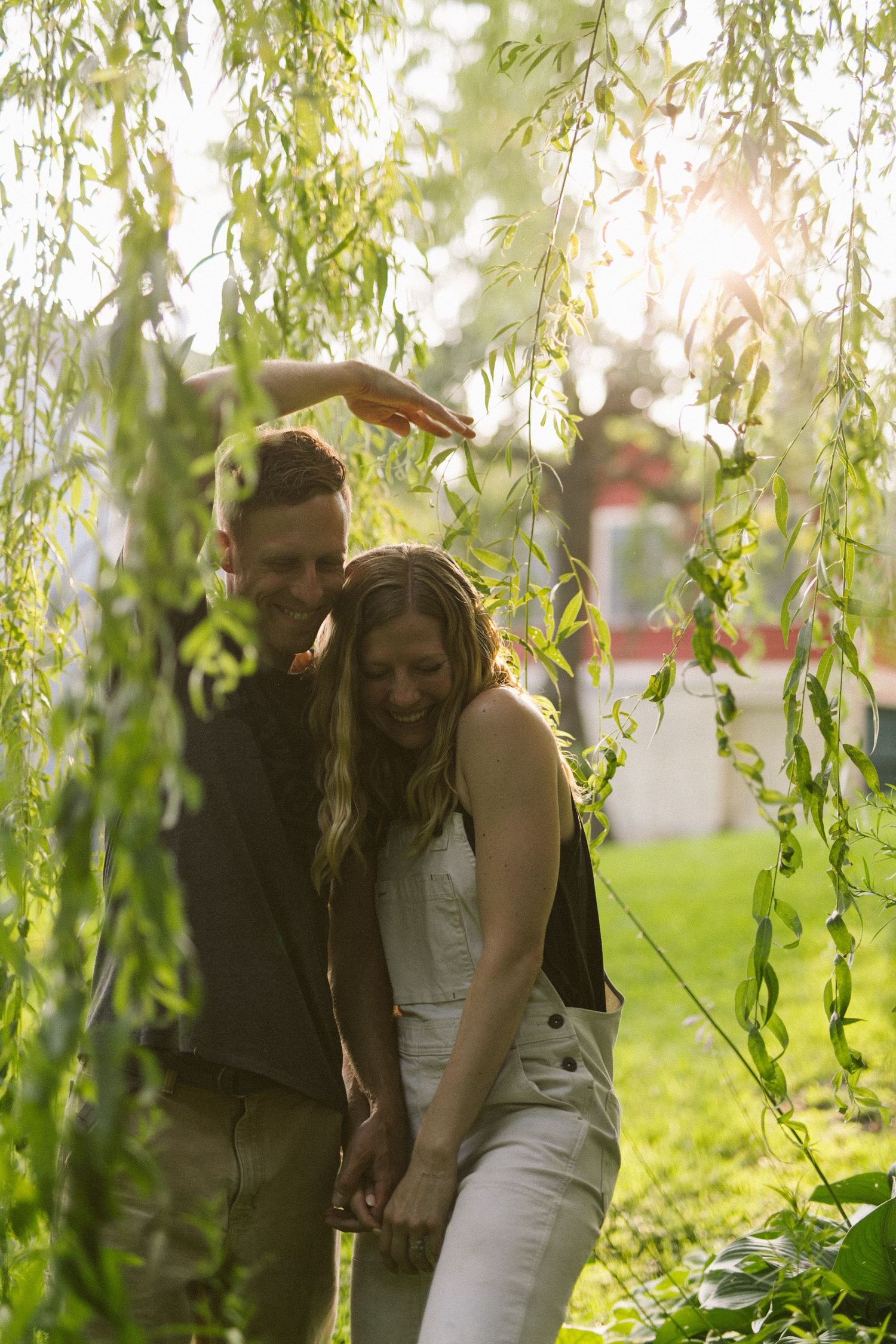 Romantic moment captured under weeping willow branches in golden sunlight.