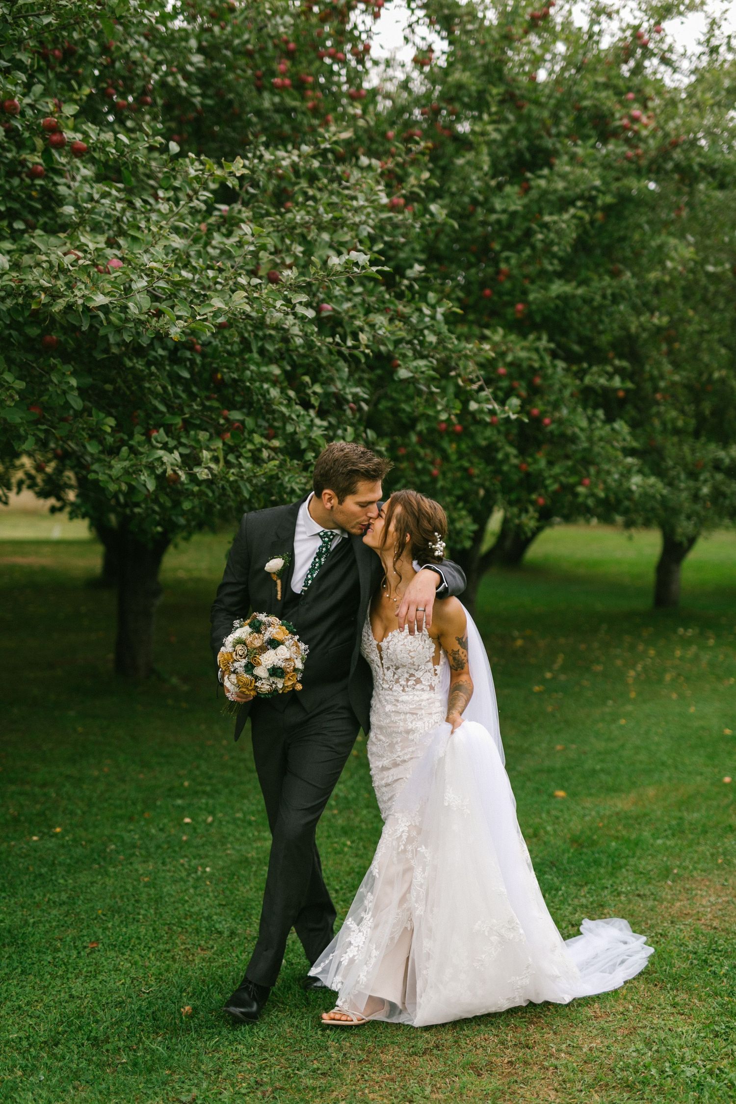 A romantic couple shares a tender moment in an apple orchard, with the bride holding a sunflower bouquet.