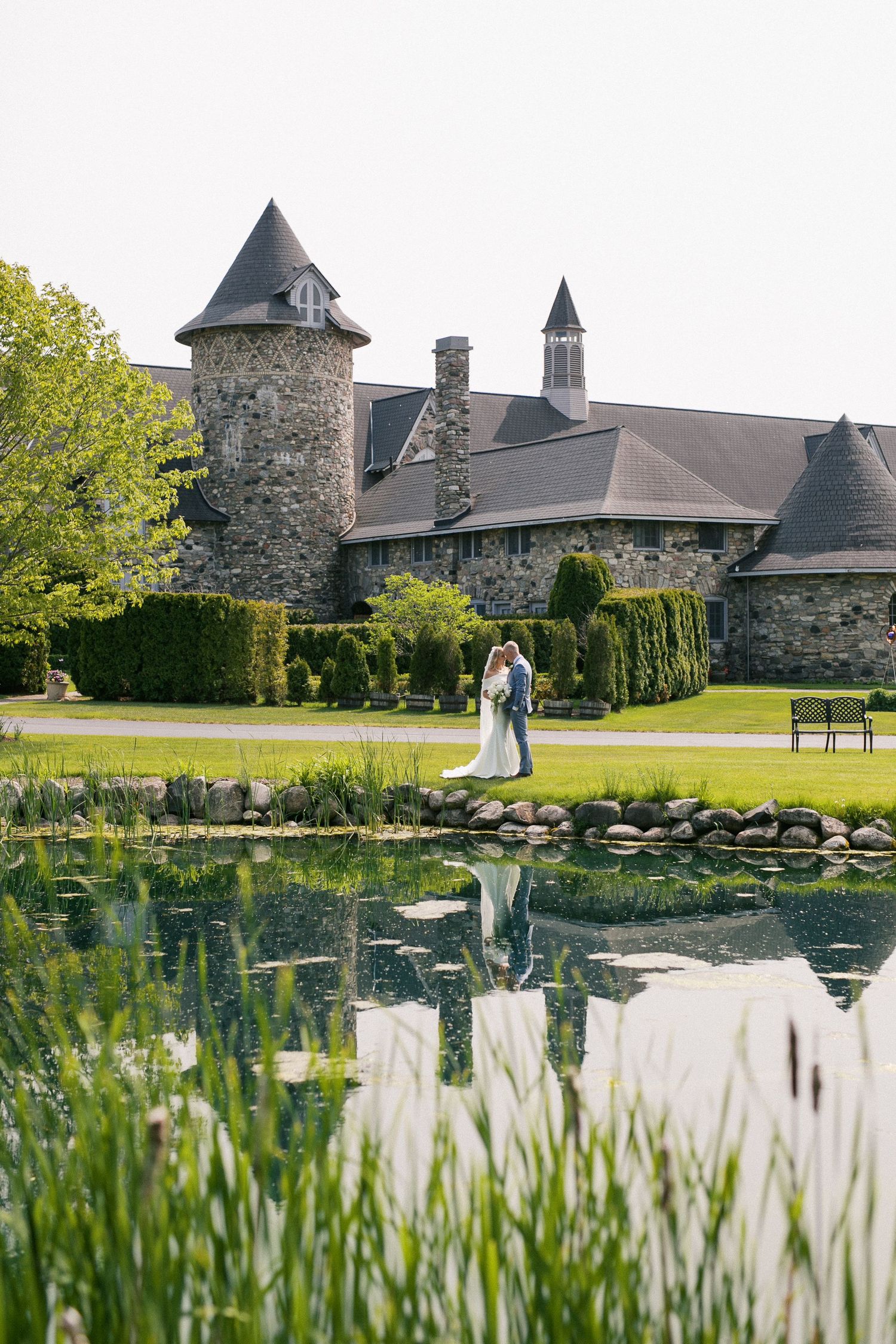 Stone castle venue with lily pond in foreground creates a romantic wedding day setting in sunlit garden.